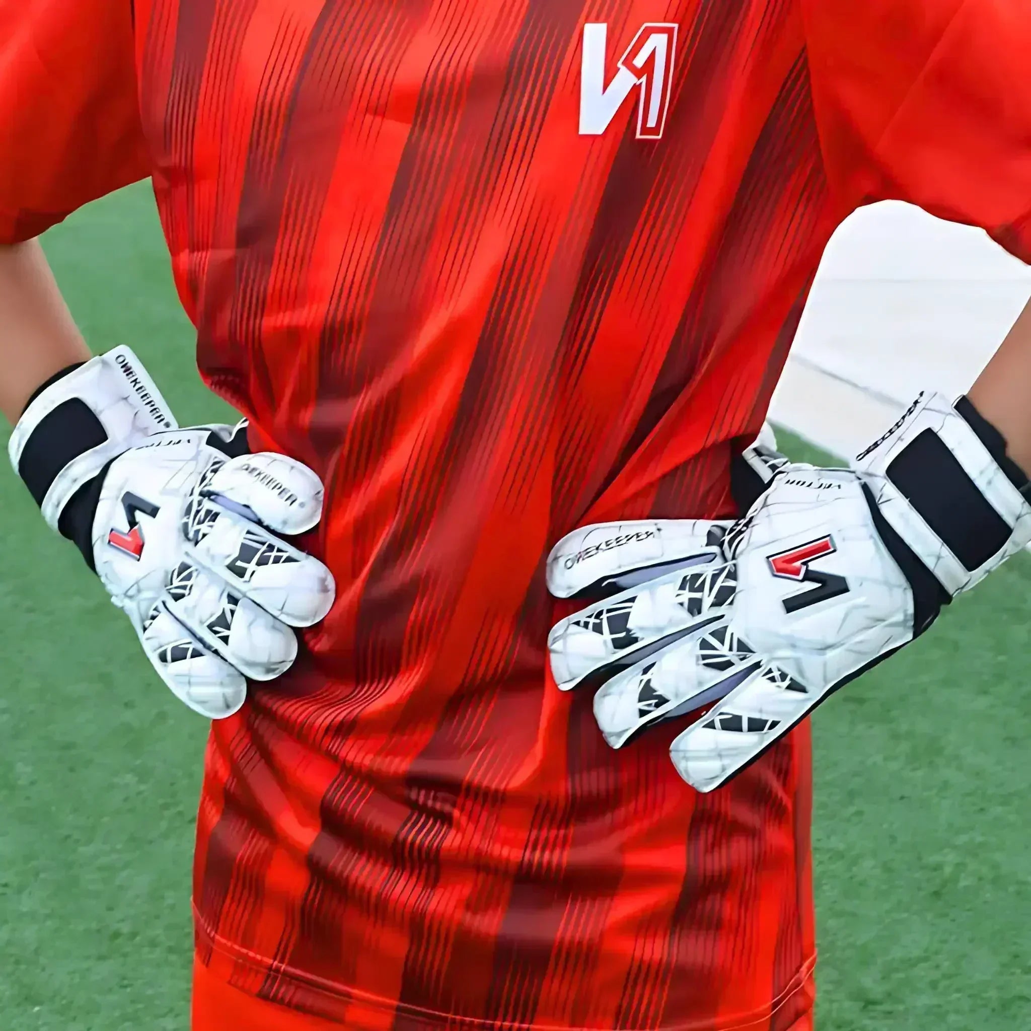 Youth goalkeeper wearing white gloves with black grip, red striped jersey on soccer field