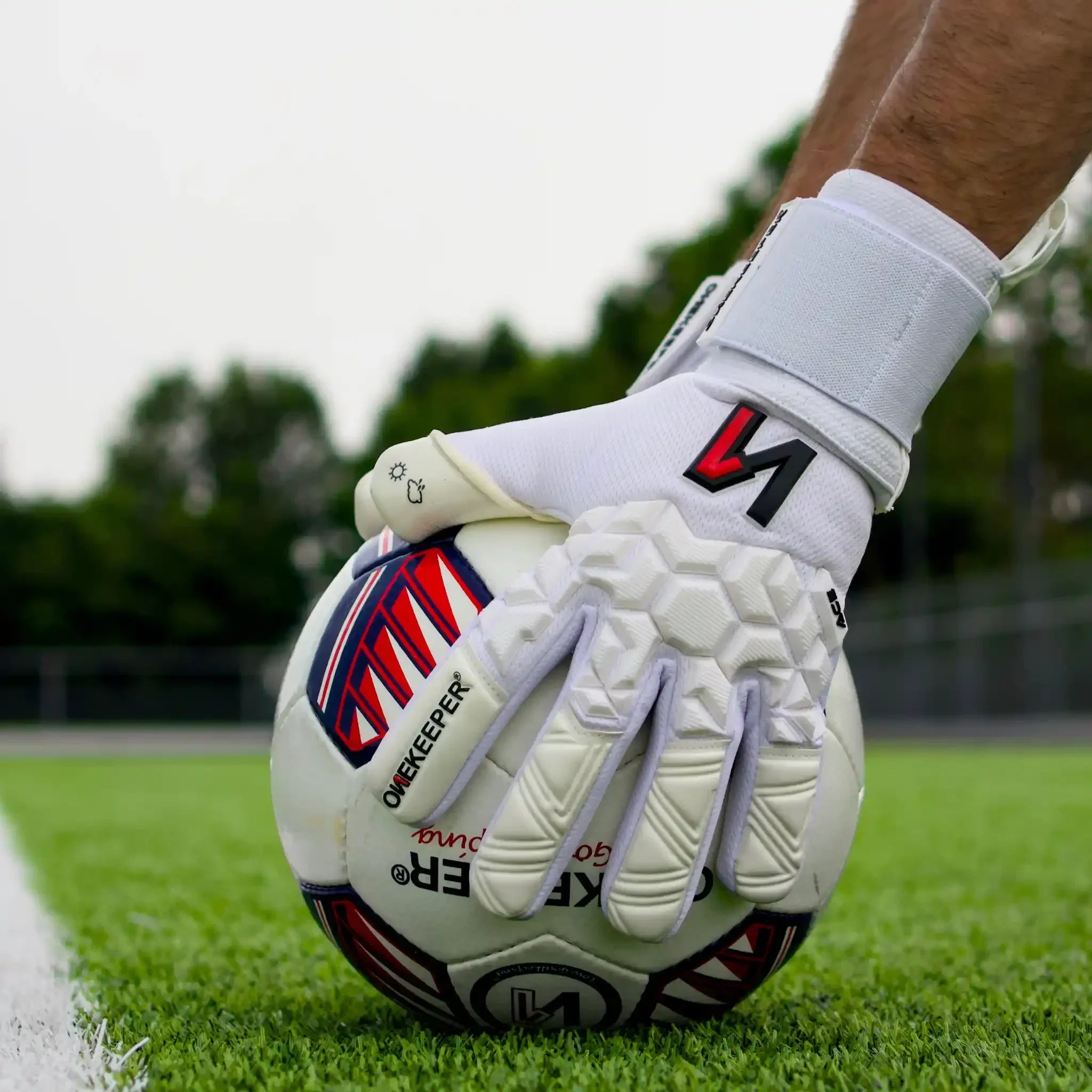 White youth goalkeeper gloves gripping soccer ball on grass field, hexagonal grip design for pro-level performance