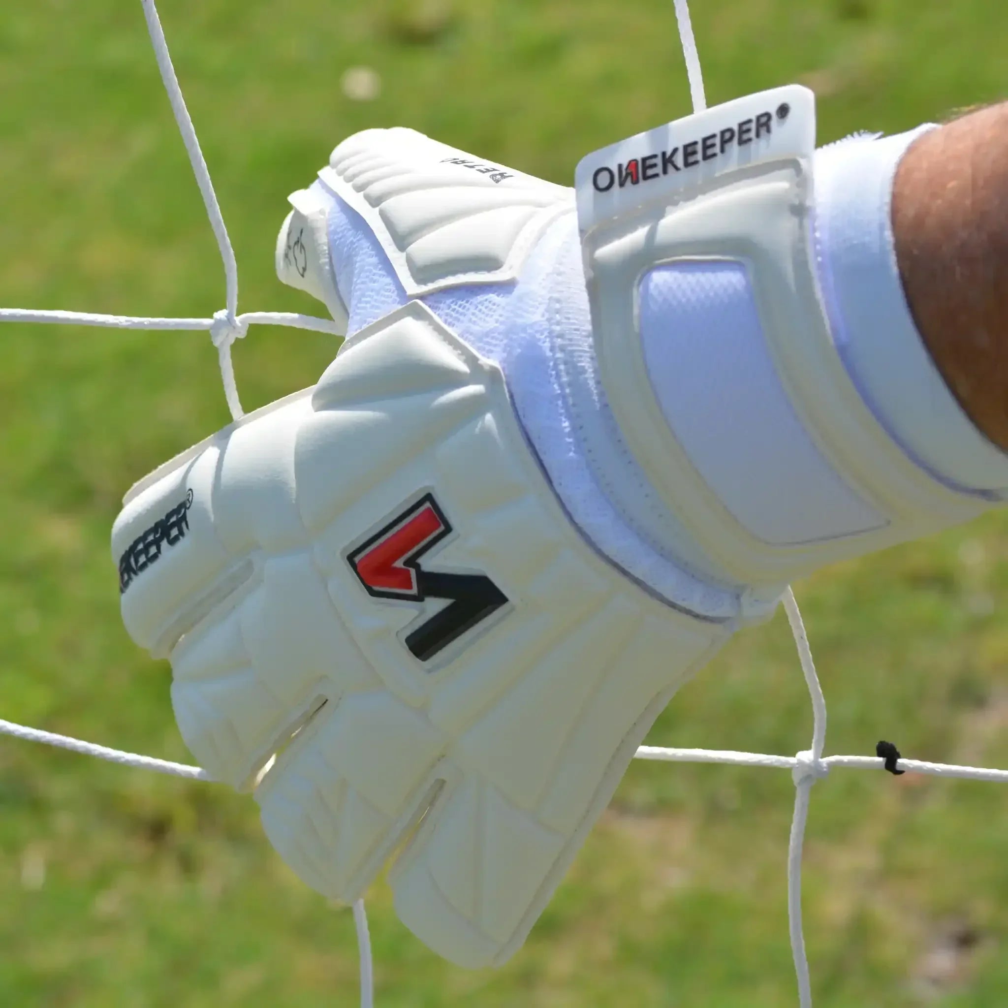 White youth goalkeeper gloves with durable grip, gripping soccer net on grass field