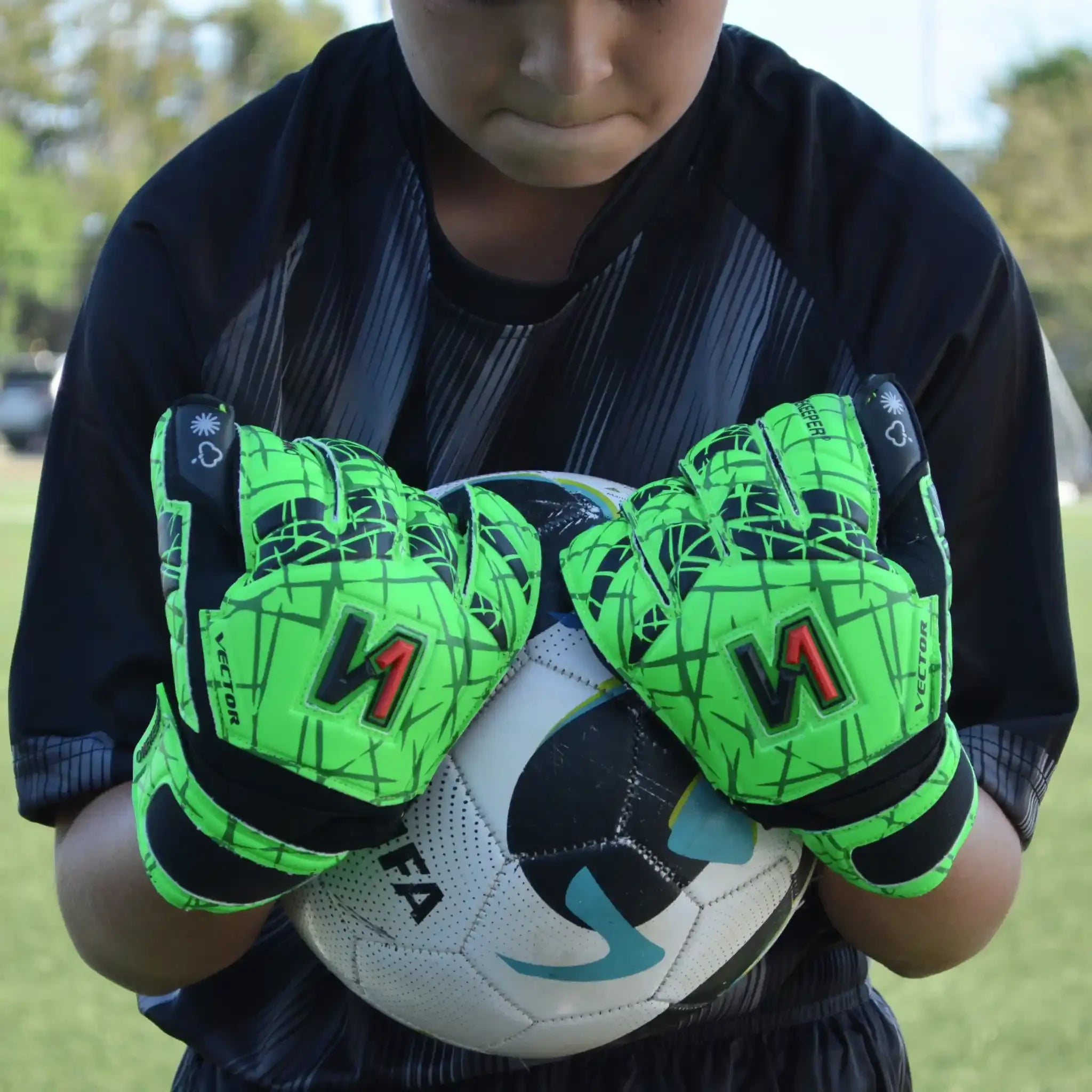 Youth goalkeeper wearing ONEKEEPER Vector Evolution neon gloves holding soccer ball on field
