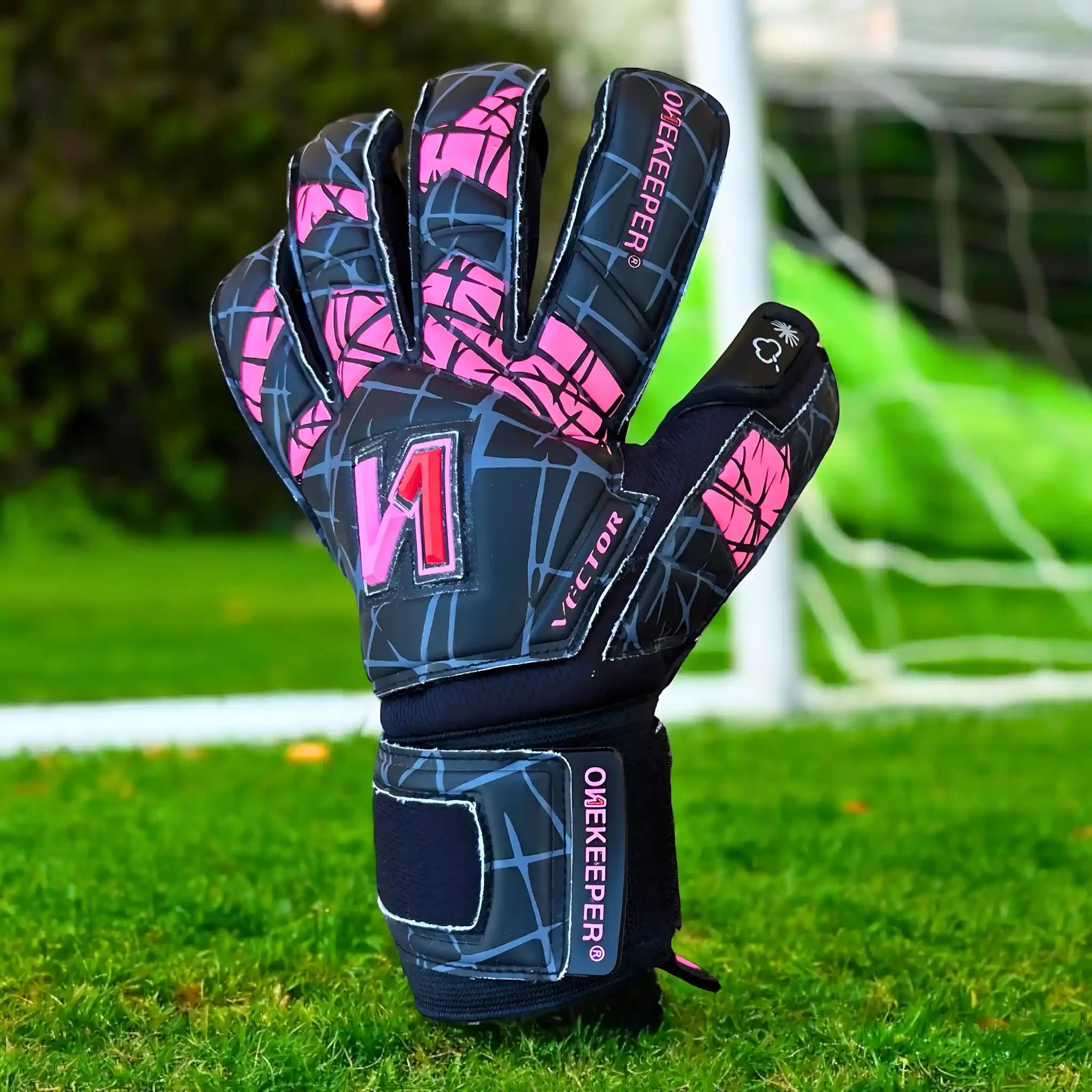 ONEKEEPER Vector Evolution Black and pink goalkeeper glove on grass with a blurred goalpost in the background