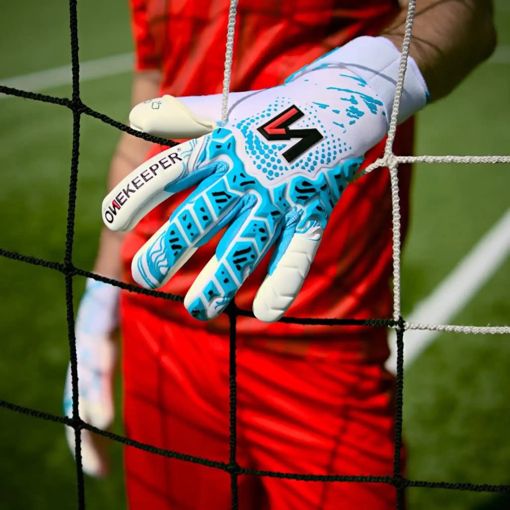 ONEKEEPER USA goalkeeper glove with blue accents gripping a soccer ball on a grass field