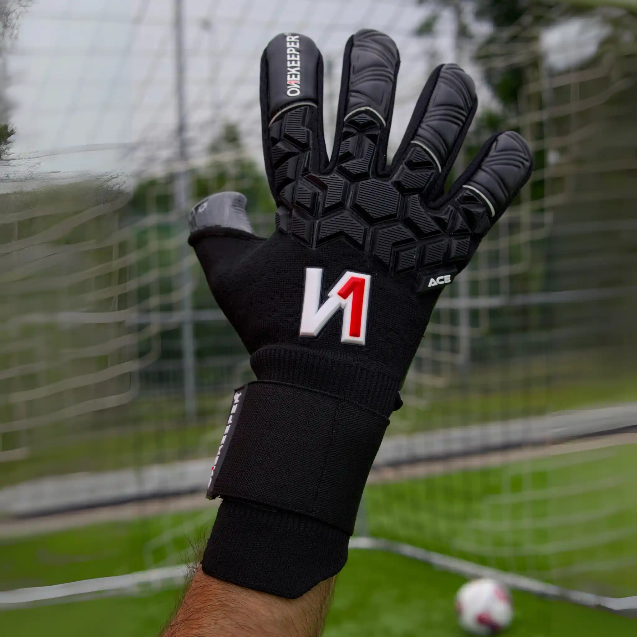 ONEKEEPER ACE Black goalkeeper glove with brand logo on a blurred soccer field background