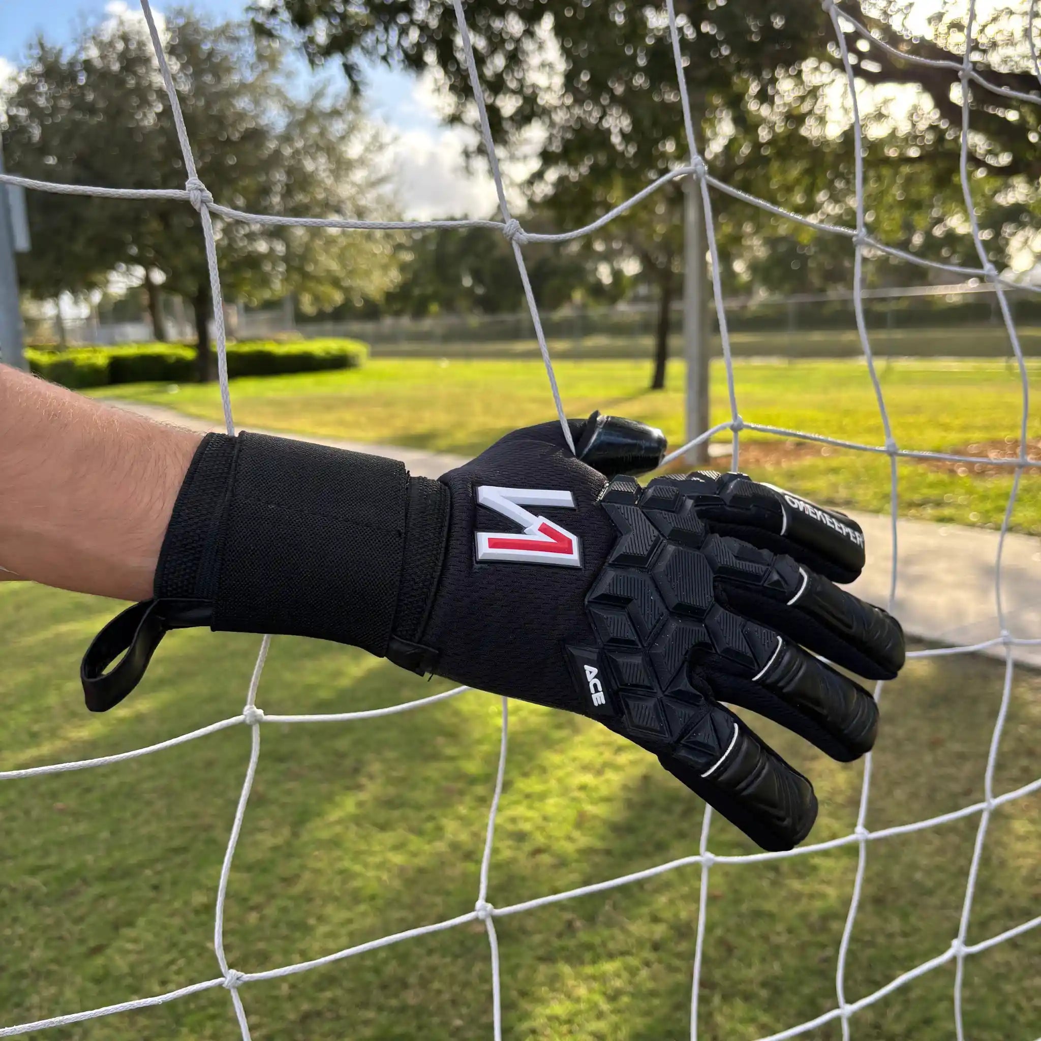 onekeeper ace Black sports glove with a logo held against a soccer goal net.