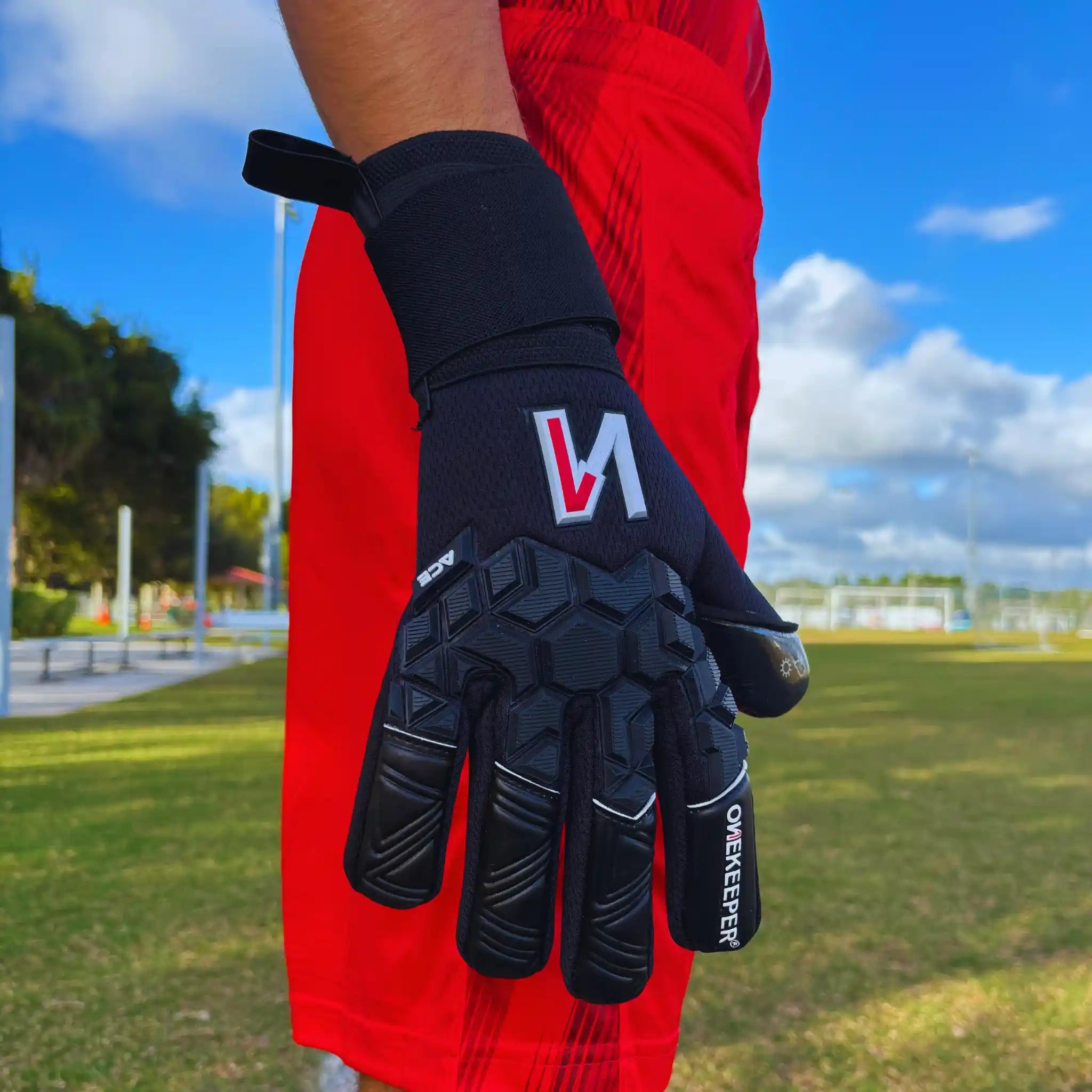 onekeeper ace Black glove with a logo on a person wearing red pants outdoors.