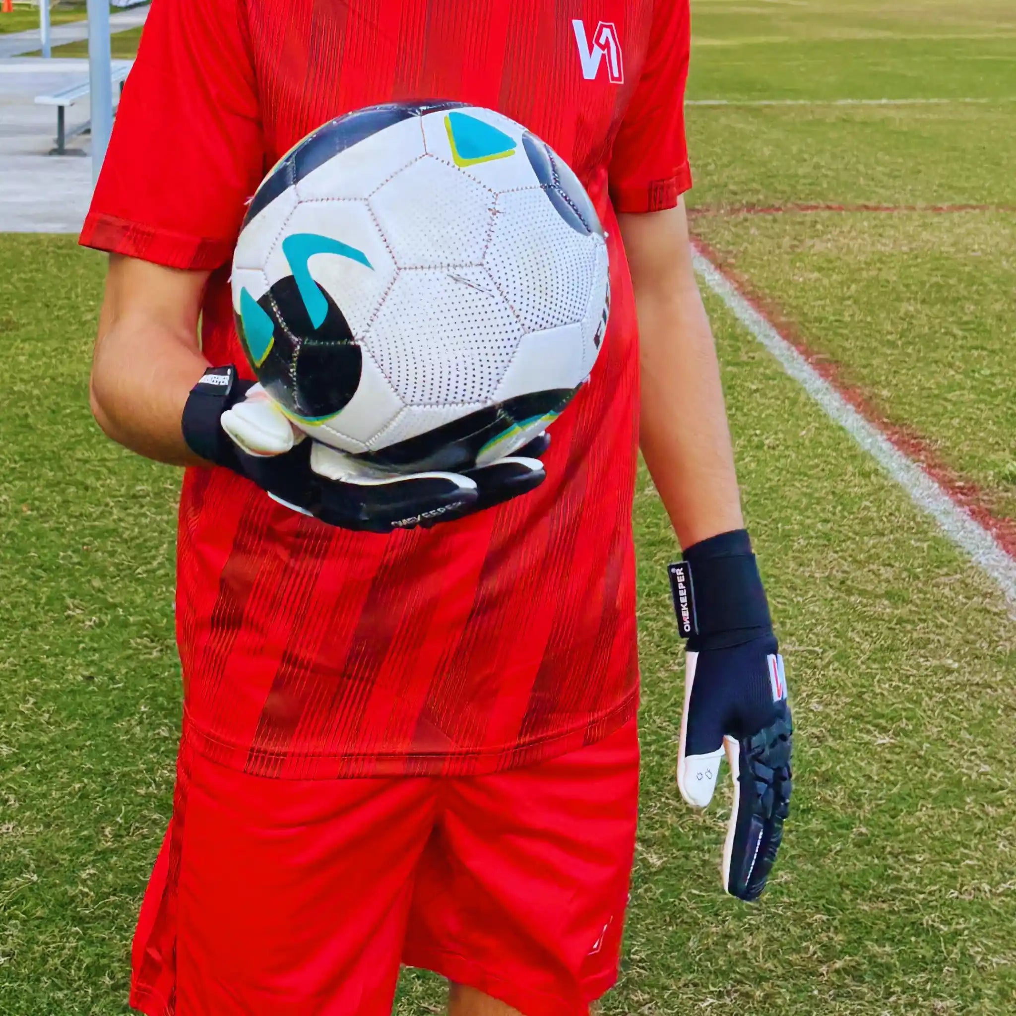 Person in red sports outfit holding a soccer ball on a grass field with the ONEKEEPER ACE Black and White