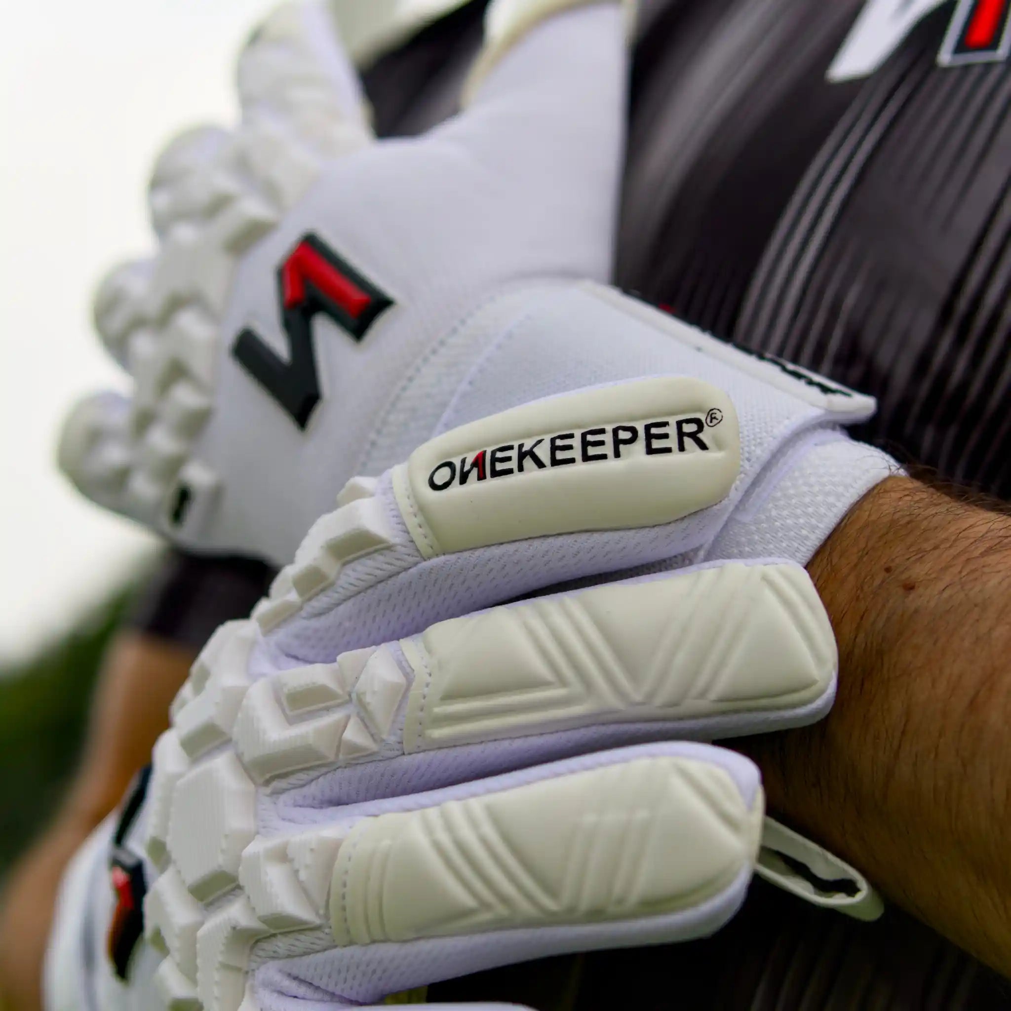 ONEKEEPER ACE White goalkeeper gloves with 'OneKeeper' branding on a blurred background