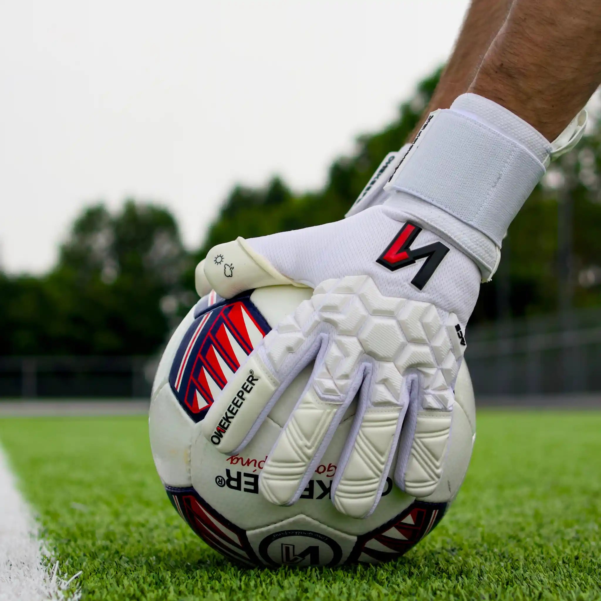 ONEKEEPER ACE White Goalkeeper glove holding a soccer ball on a grass field