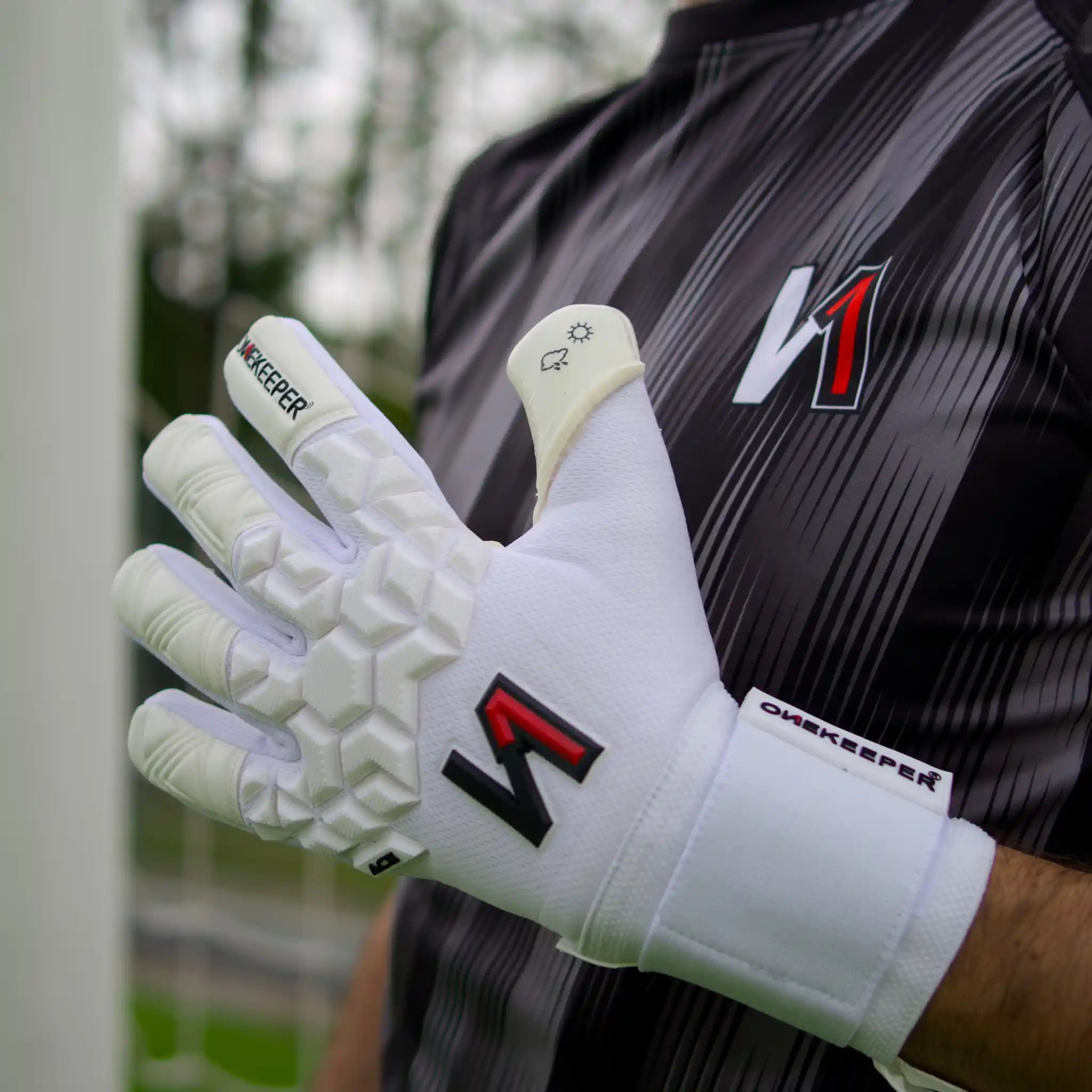 ONEKEEPER ACE White goalkeeper gloves with visible branding worn by a person in a sports uniform.