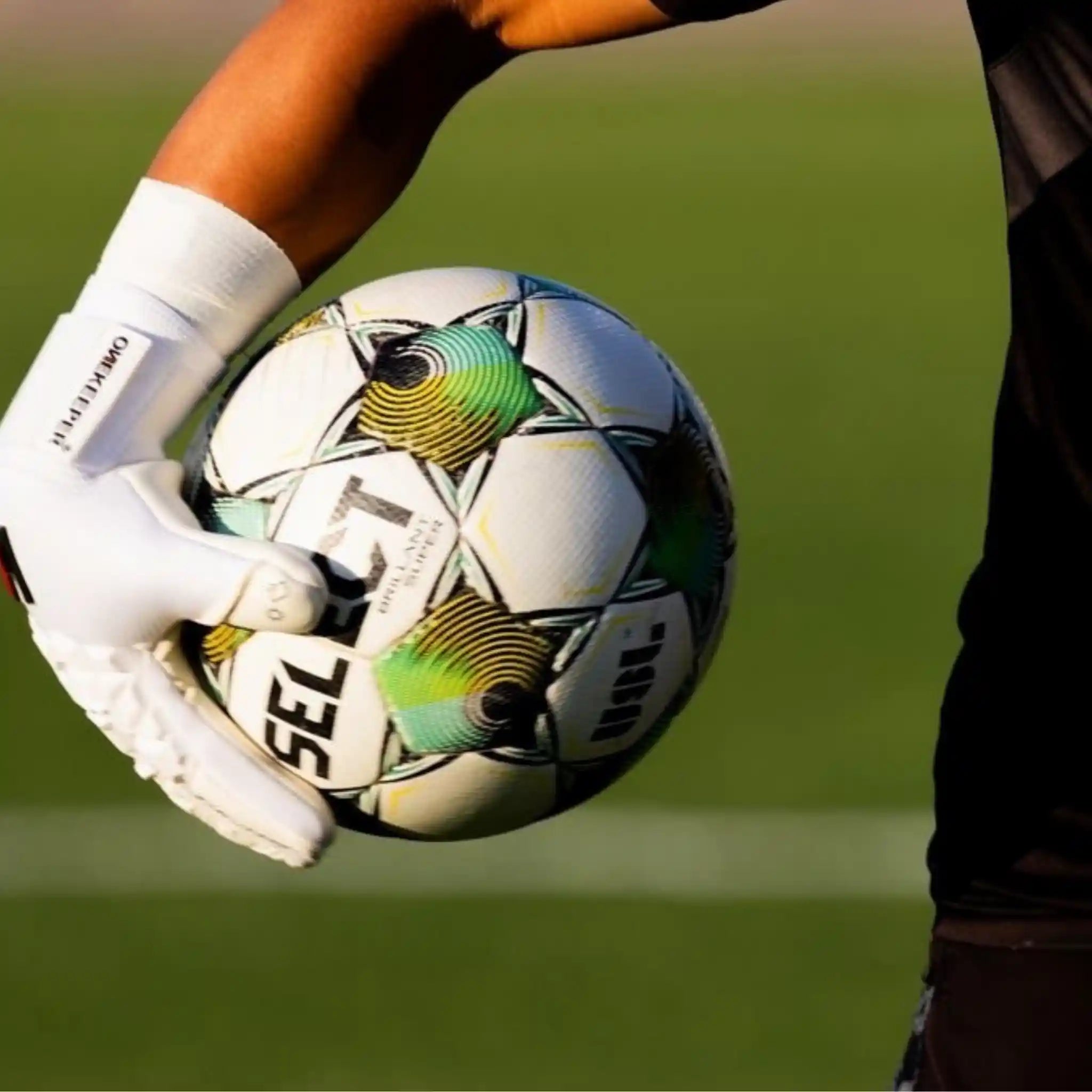 Person wearing a ONEKEEPER ACE white glove holding a soccer ball on a grass field