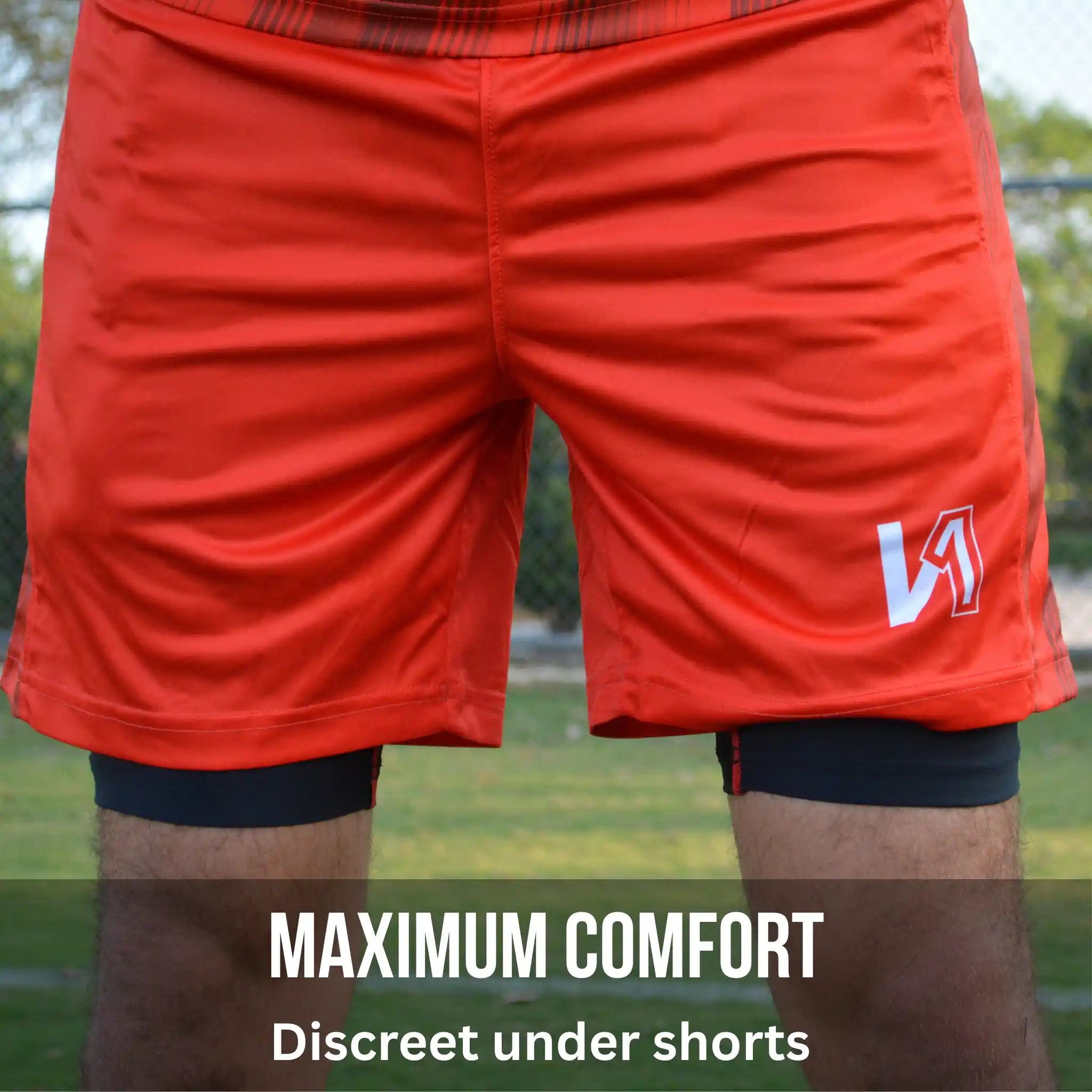 Red athletic shorts with a logo on a blurred outdoor background and a compression-padded short underneath