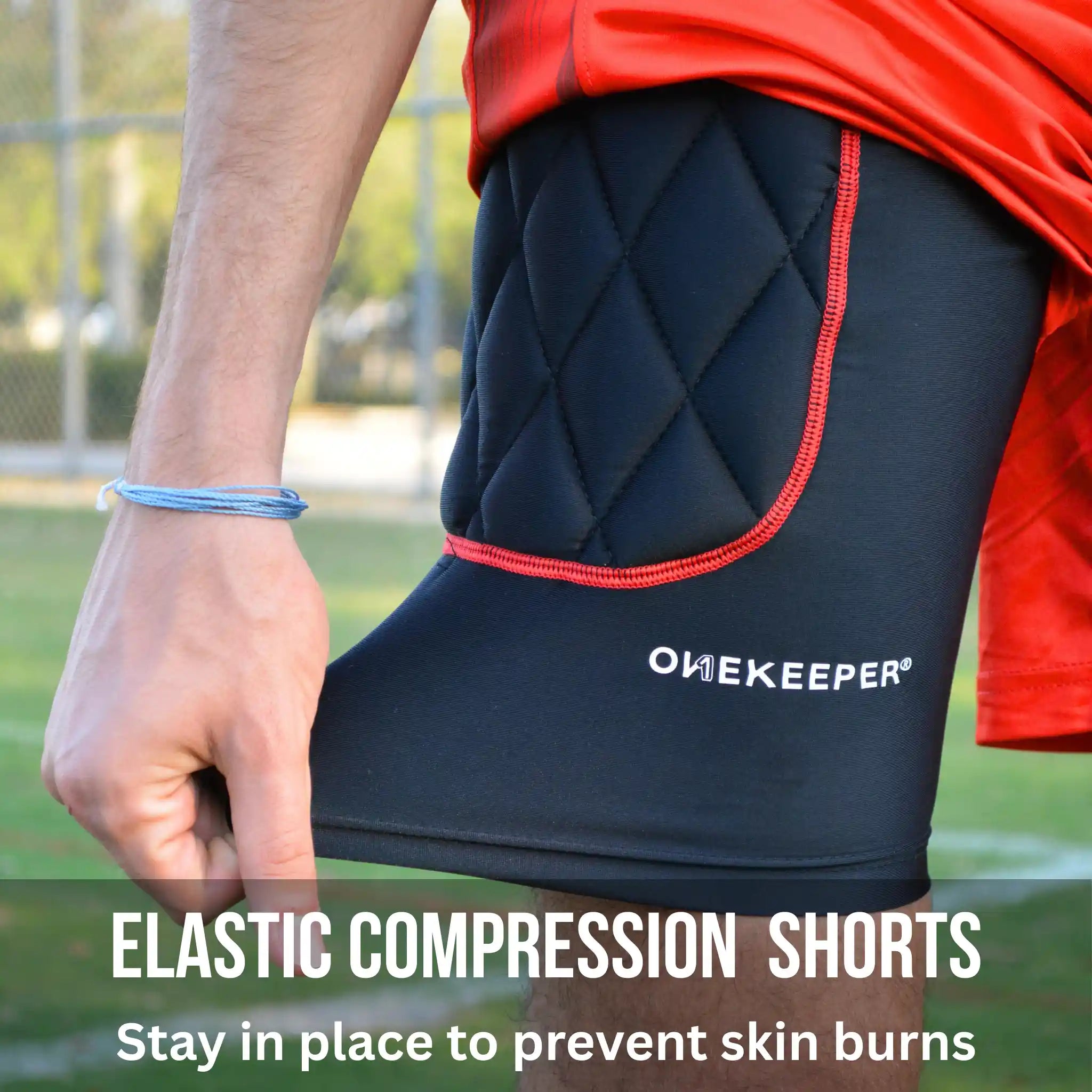 Person wearing black compression shorts with red trim on a sports field, featuring the brand 'ONEKEEPER'.