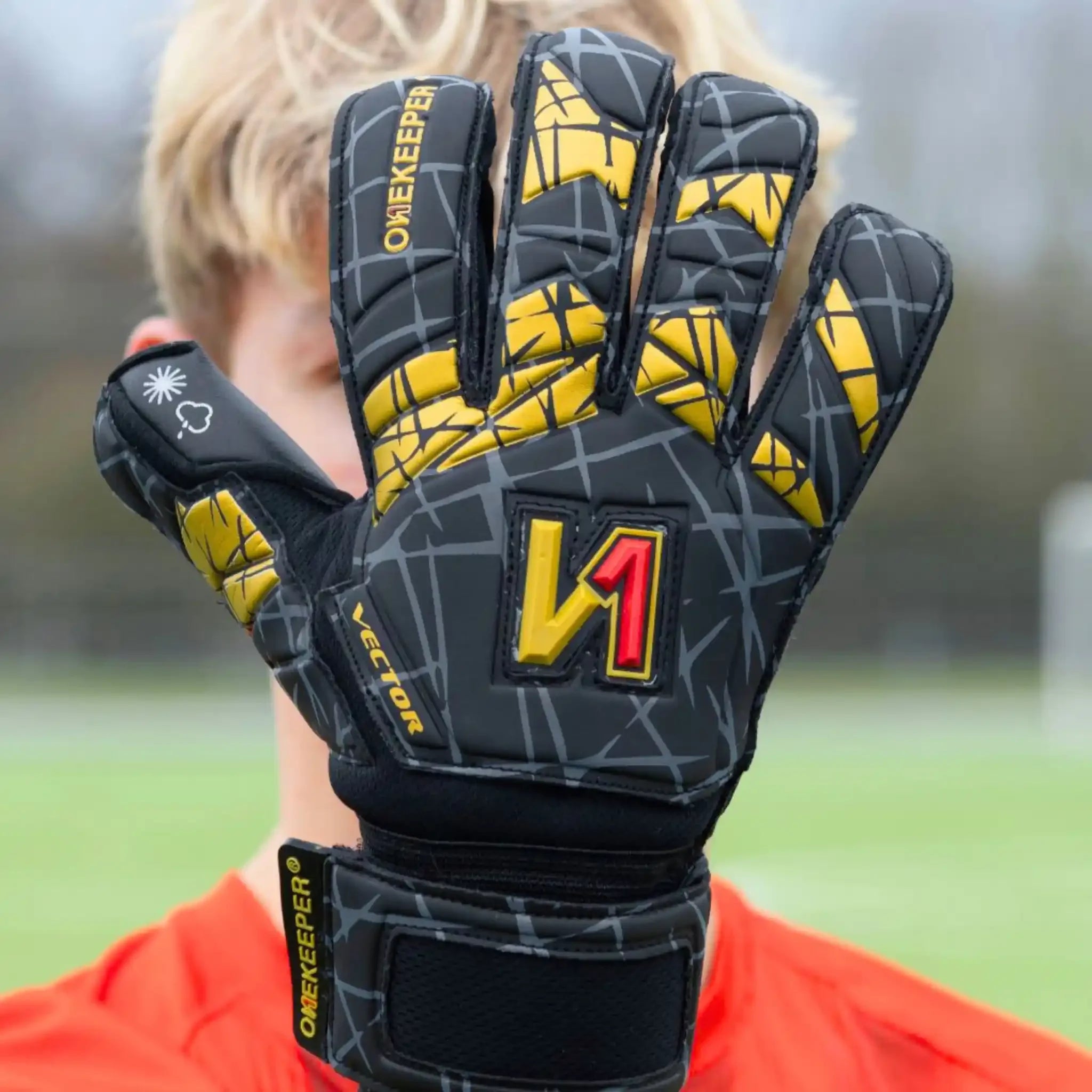 Onekeeper Black and gold goalkeeper glove with visible branding on a blurred sports field background