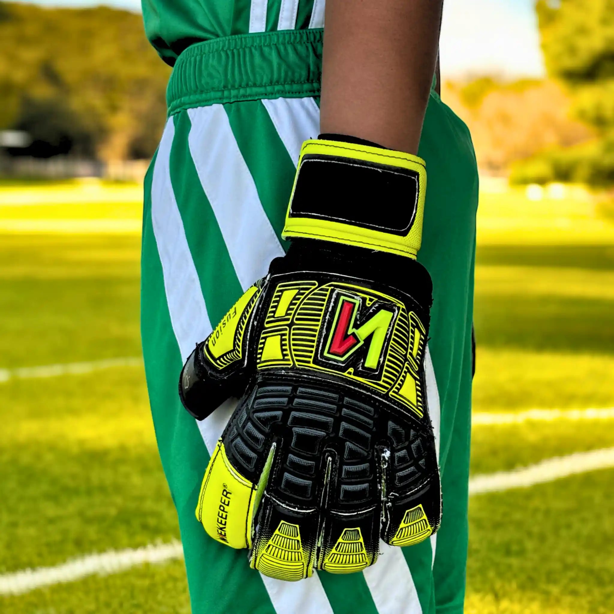 Person wearing a onekeeper fusion green and white sports uniform with black and yellow gloves on a grassy field.