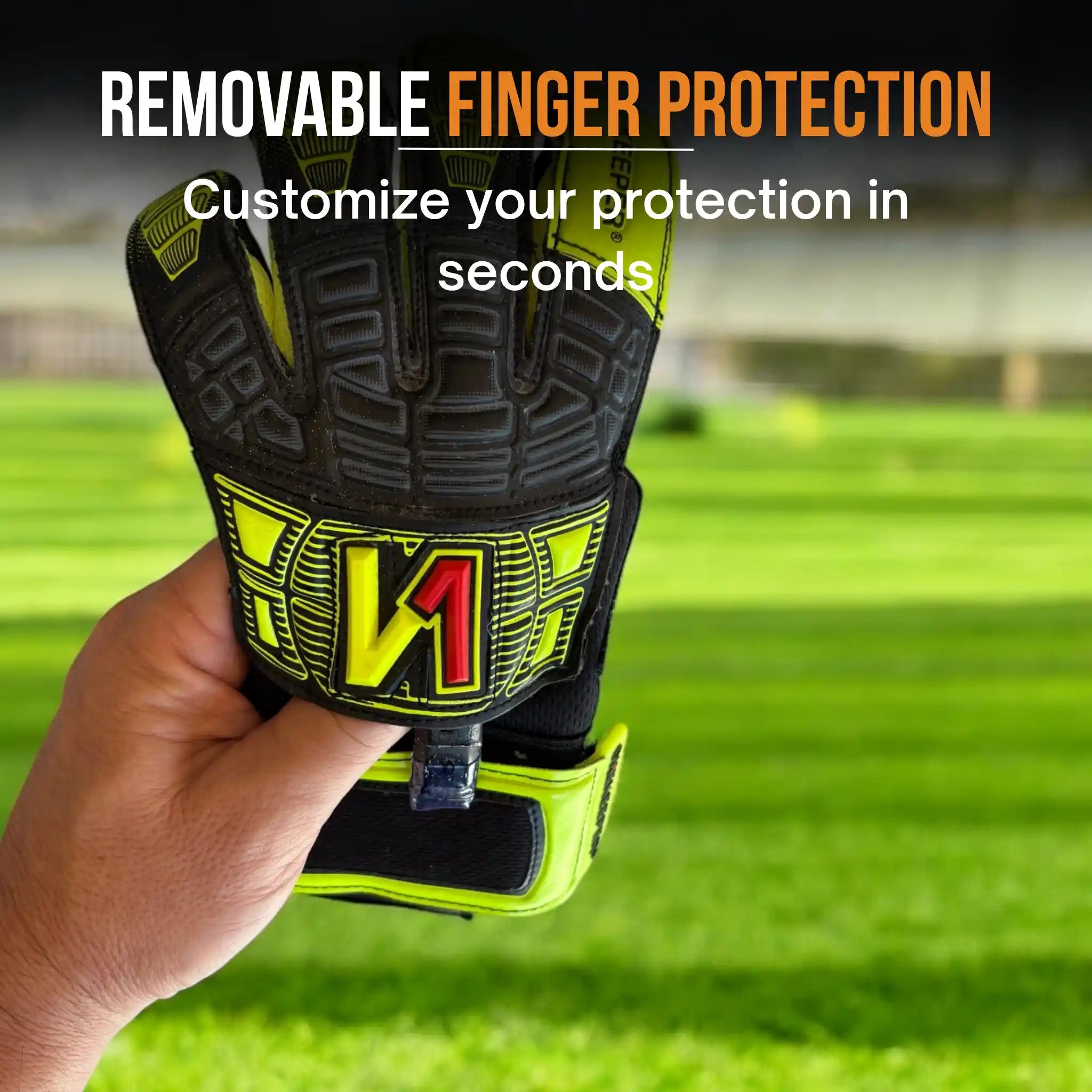 Hand holding a onekeeper fusion black and yellow glove with removable finger protection on a grass field background.