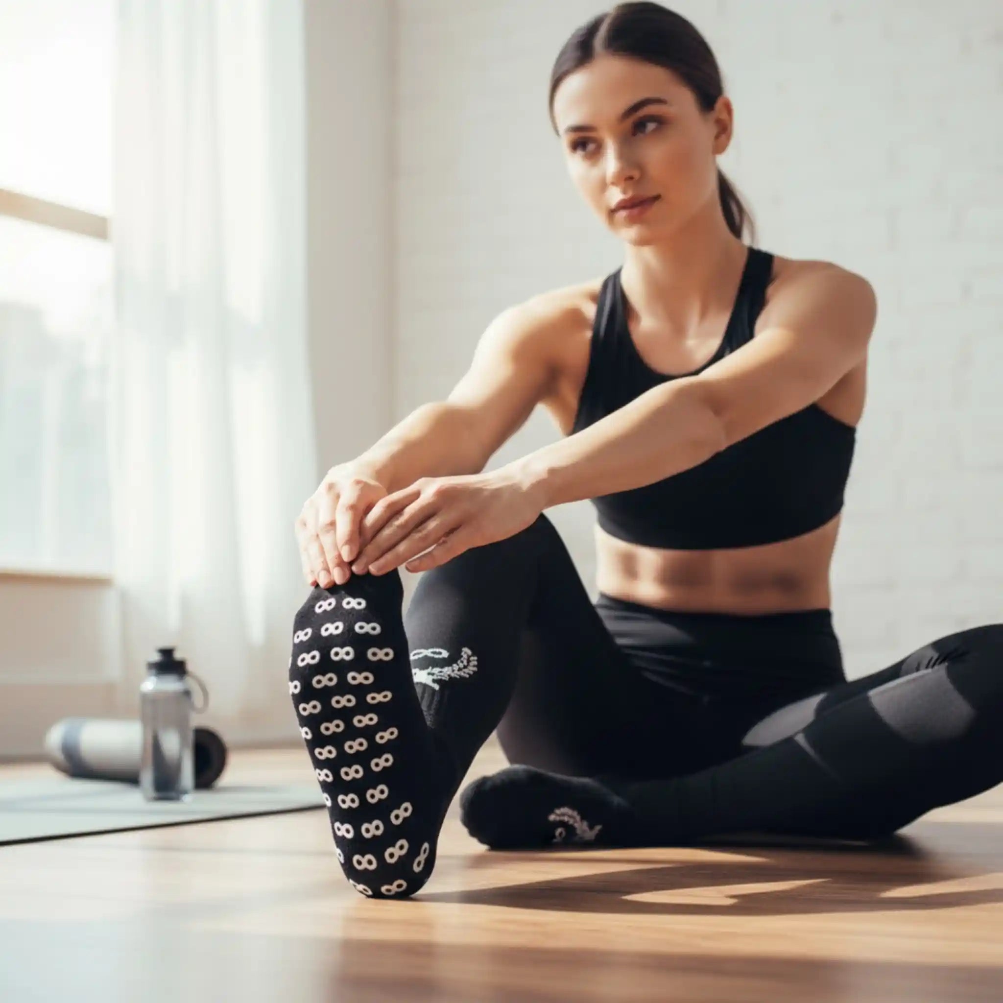 Woman stretching with a pilates ring in a bright room with a black grip socks