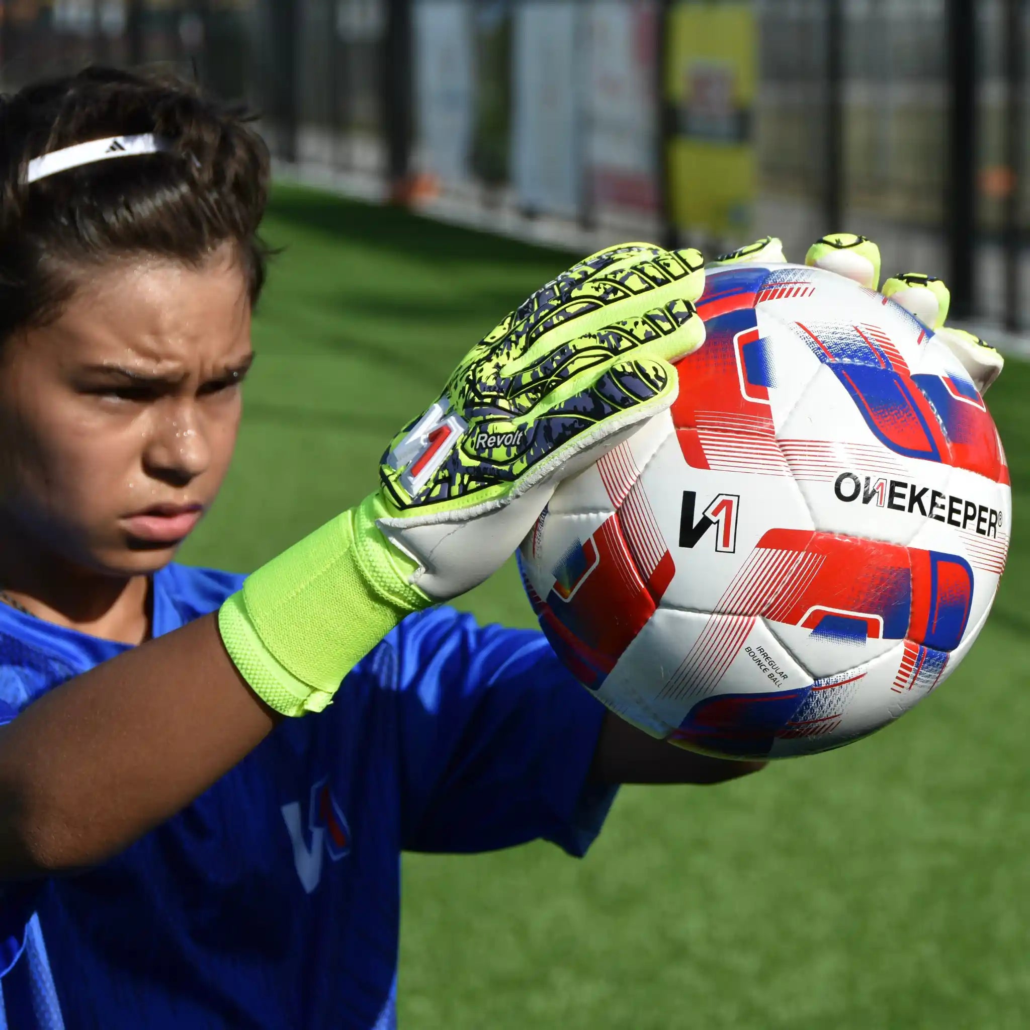Kid in goalkeeper gloves holding a soccer ball on a grass field