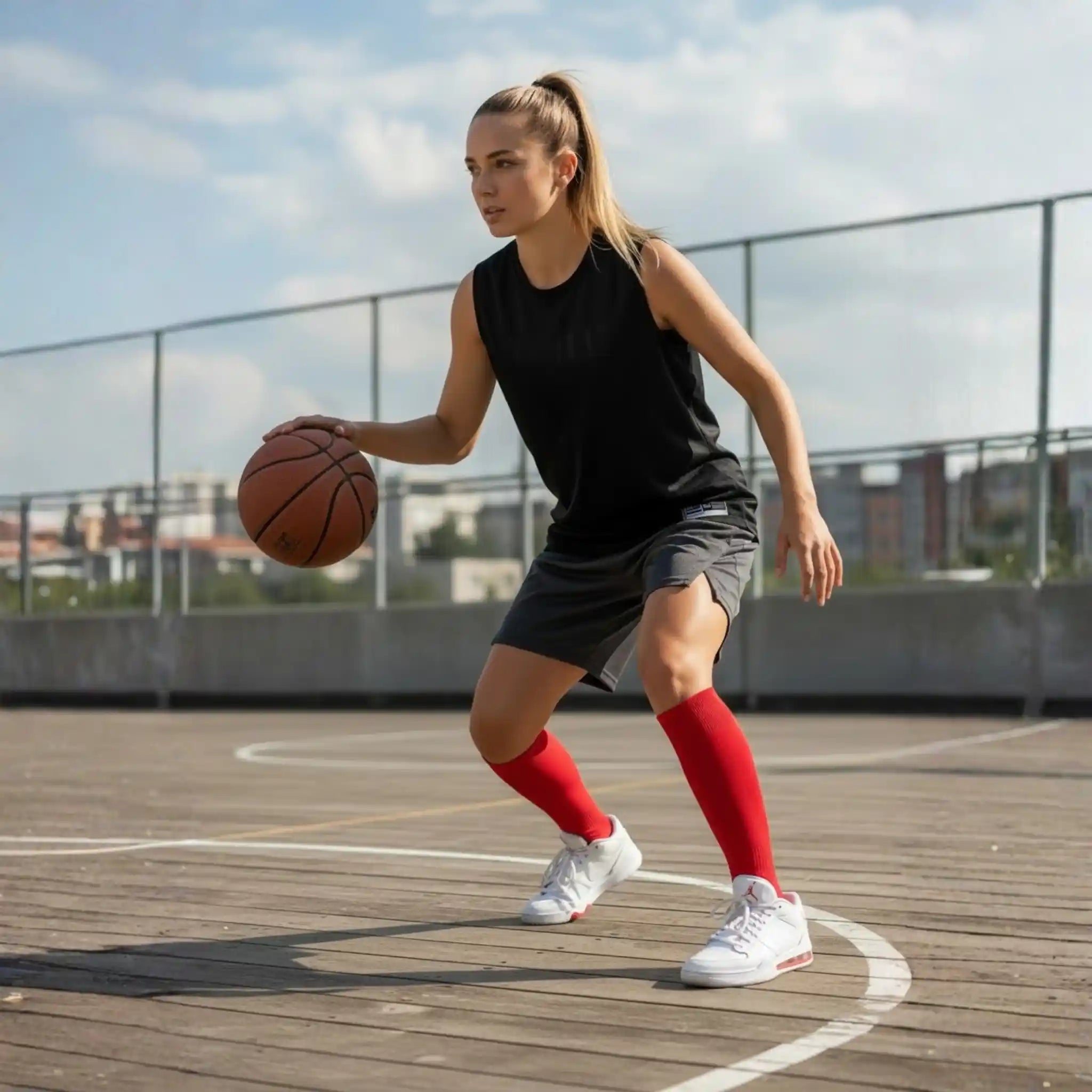 Person holding a basketball on an outdoor court with a clear sky, wearing a red onekeeper long grip sock