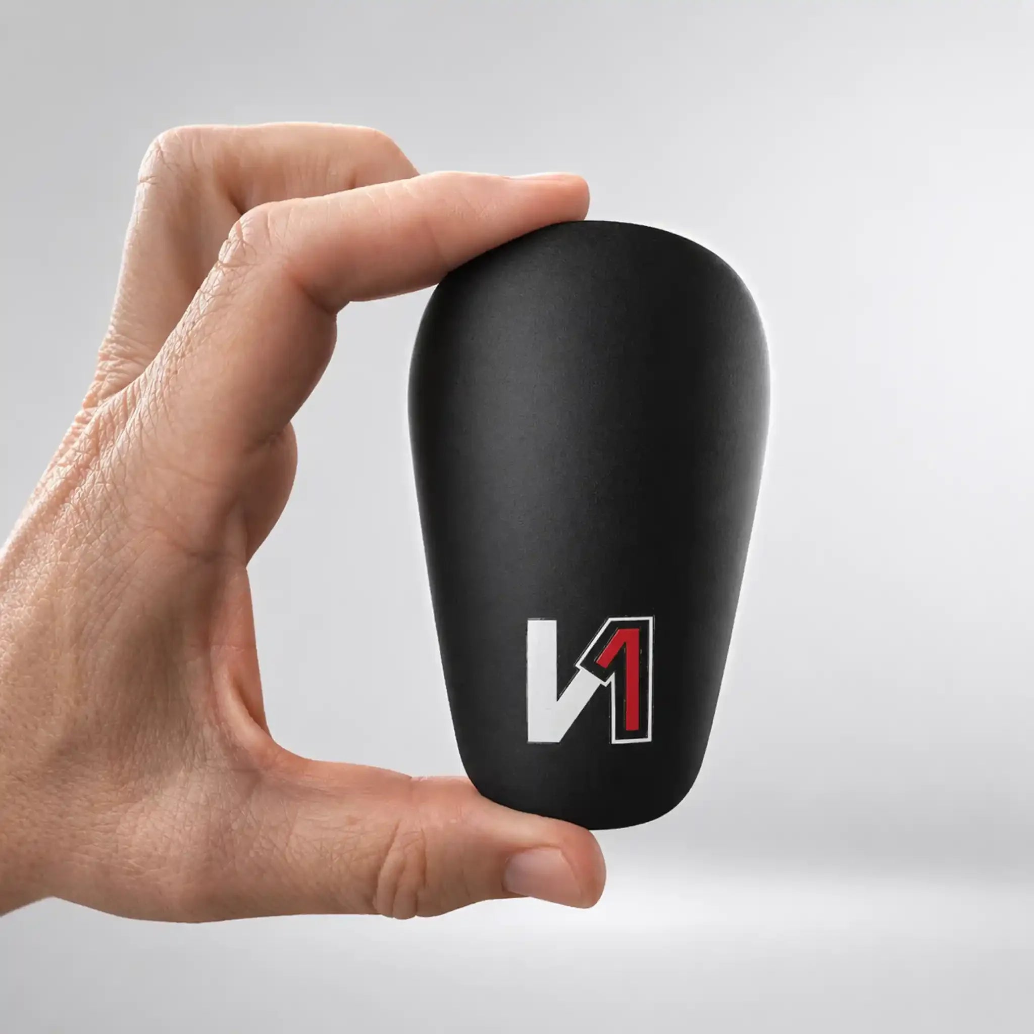 Hand holding a black mini shin guard with a red and white logo, soccer gear accessory