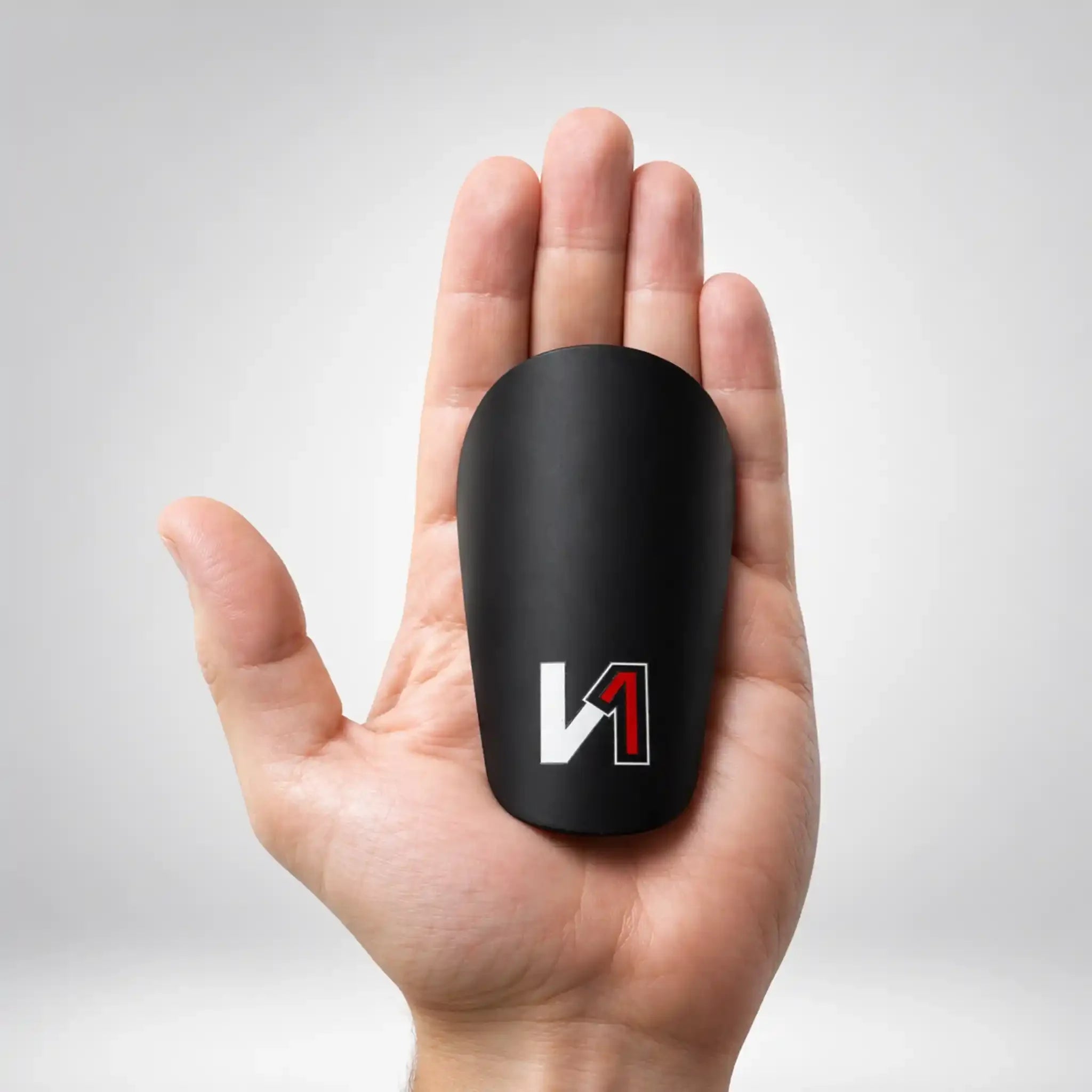 Small black soccer shin guard with white and red logo shown in an open palm
