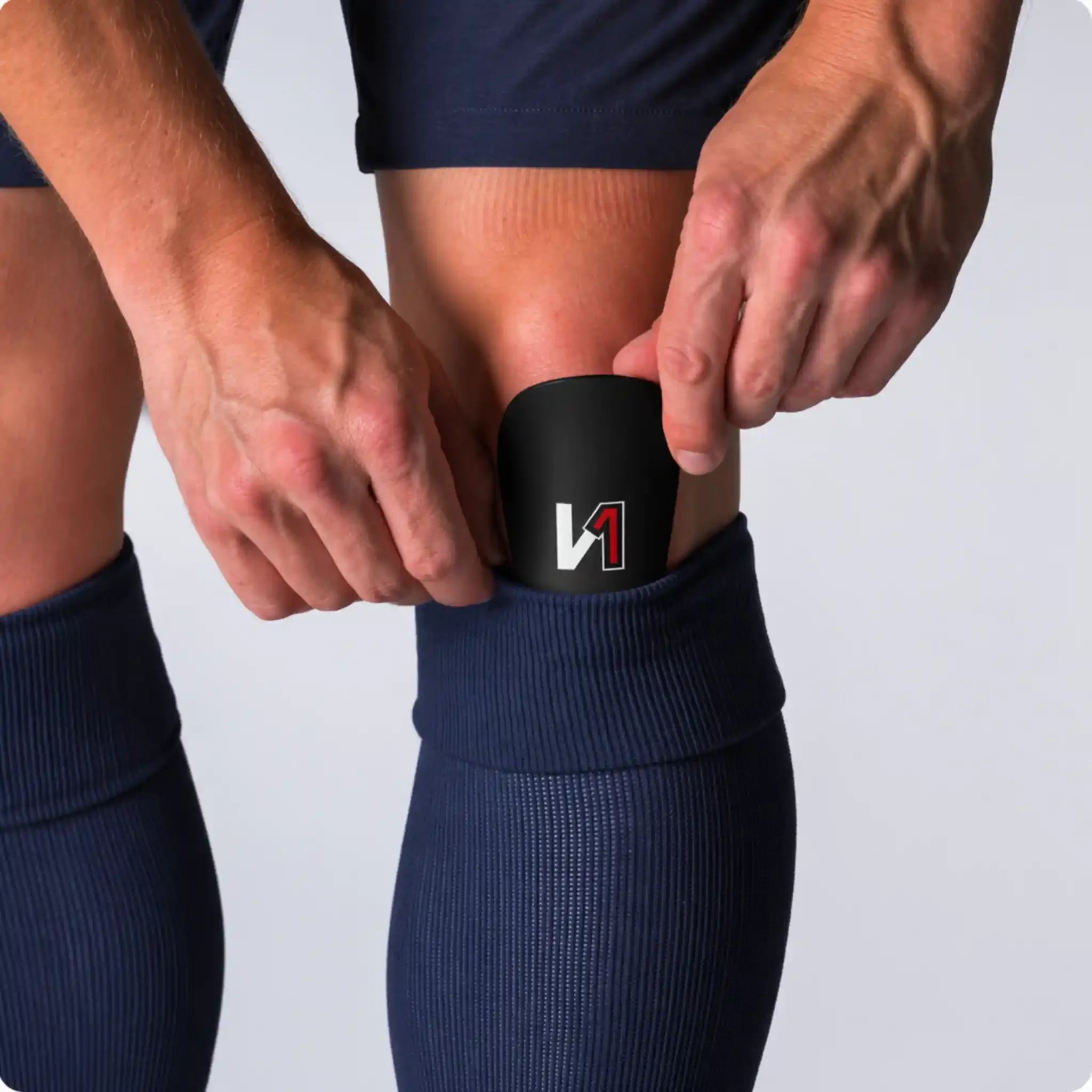 Person inserting a black mini soccer shin guard with logo into navy blue sock
