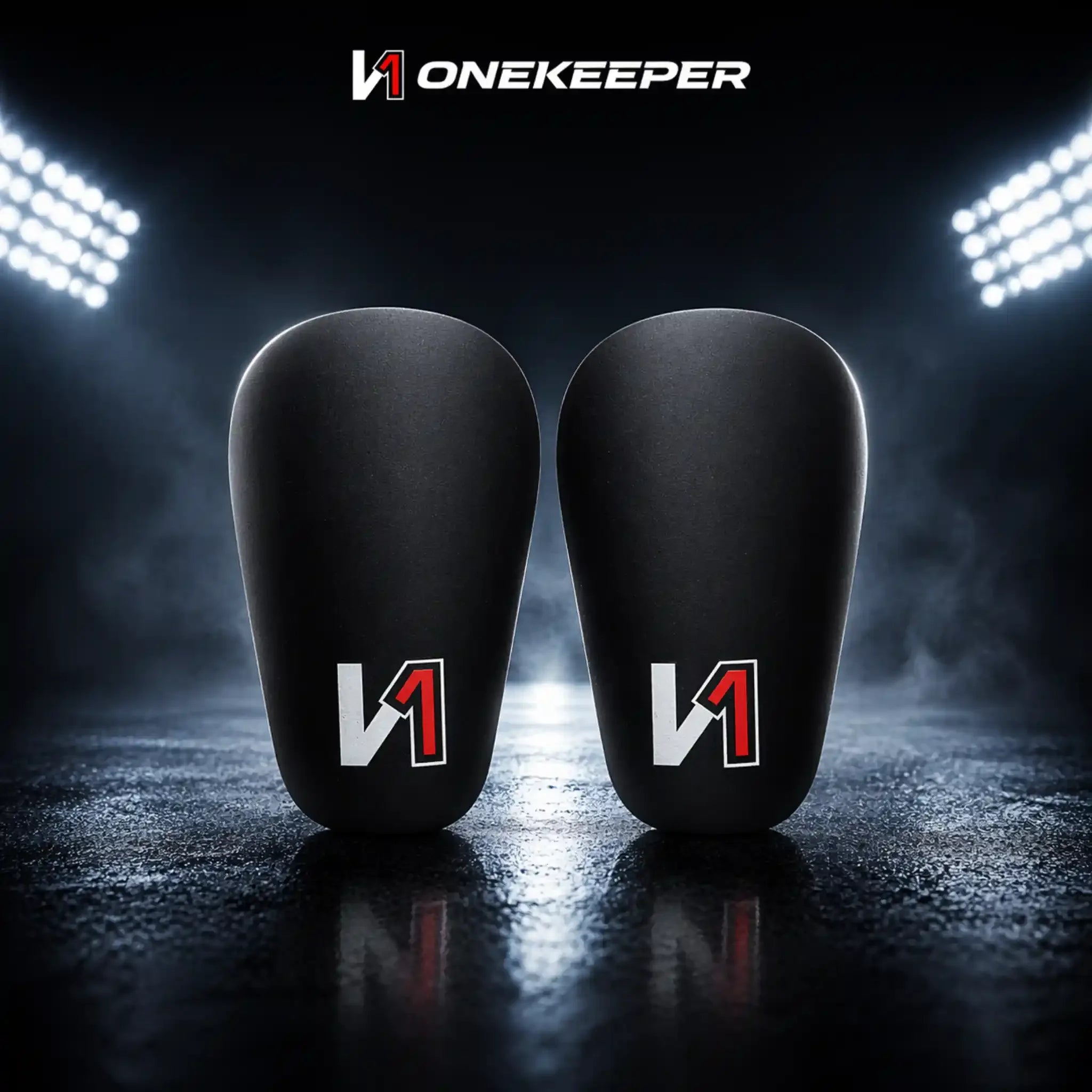 Pair of black mini shin guards with red and white logo, on dark stadium background