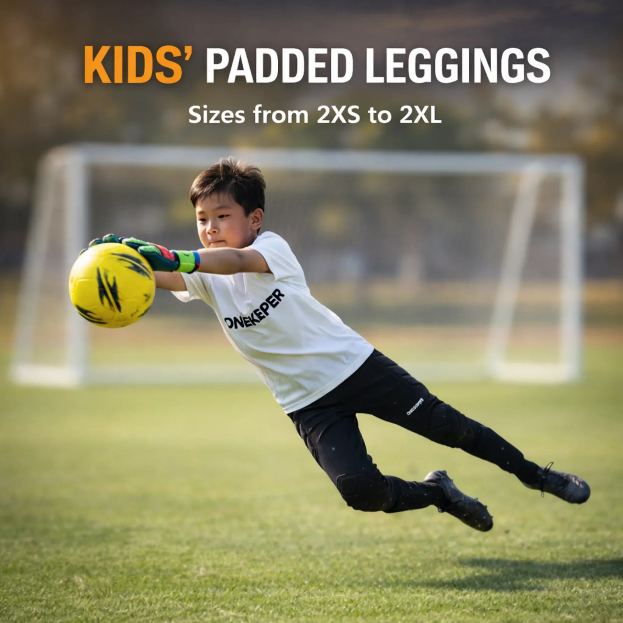 Young soccer goalkeeper in ONEKEEPER padded leggings diving to catch a yellow ball on a grass field