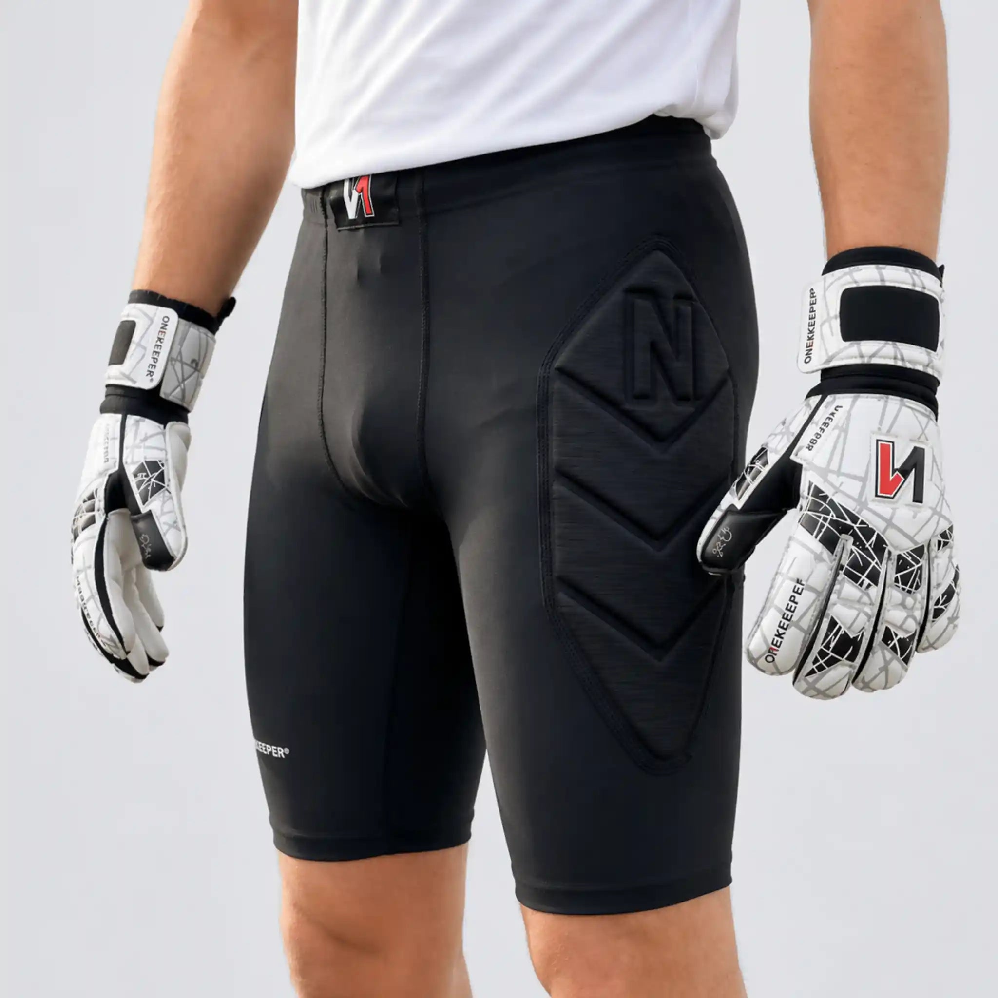 Person wearing a onekeeper black protective shorts with a brand logo, white gloves with black accents, on a light gray background.