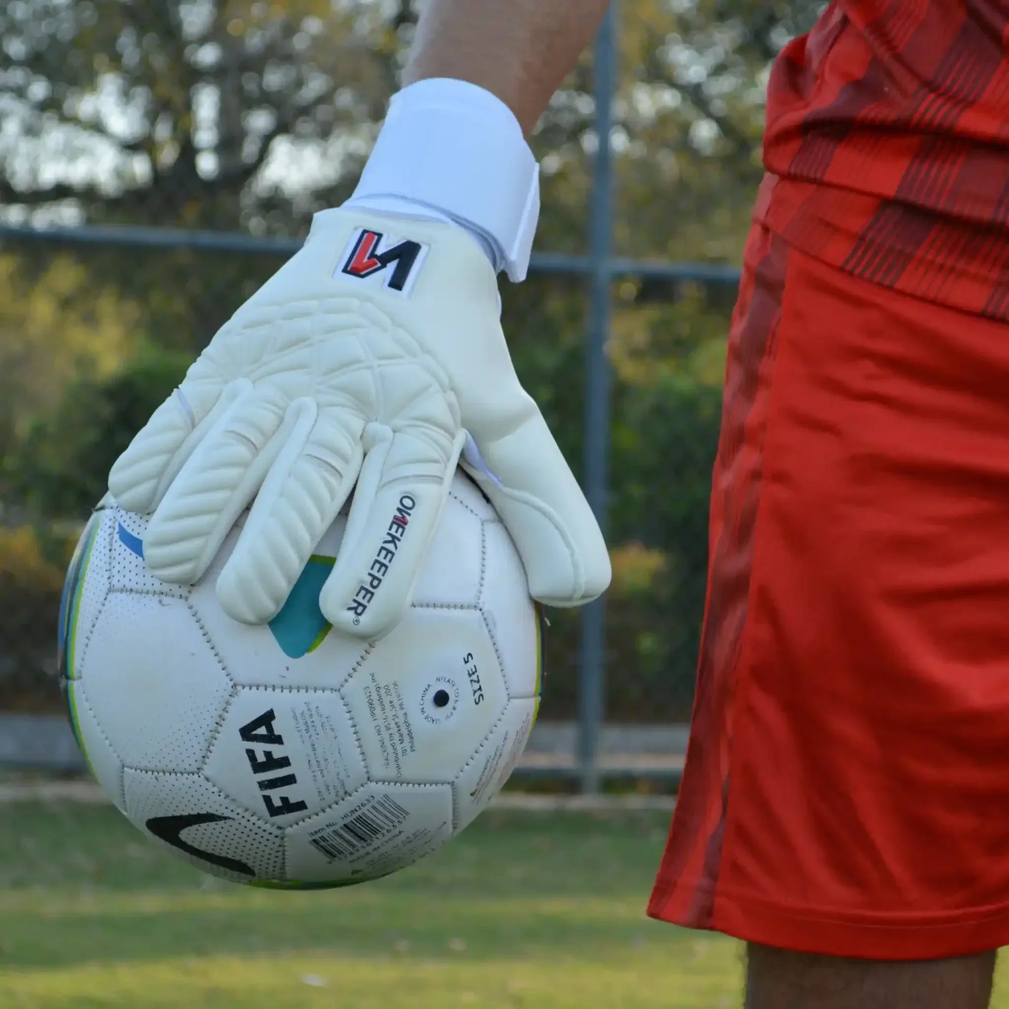 Goalkeeper wearing a onekeeper philipp kohn white gloves holding FIFA soccer ball on outdoor field