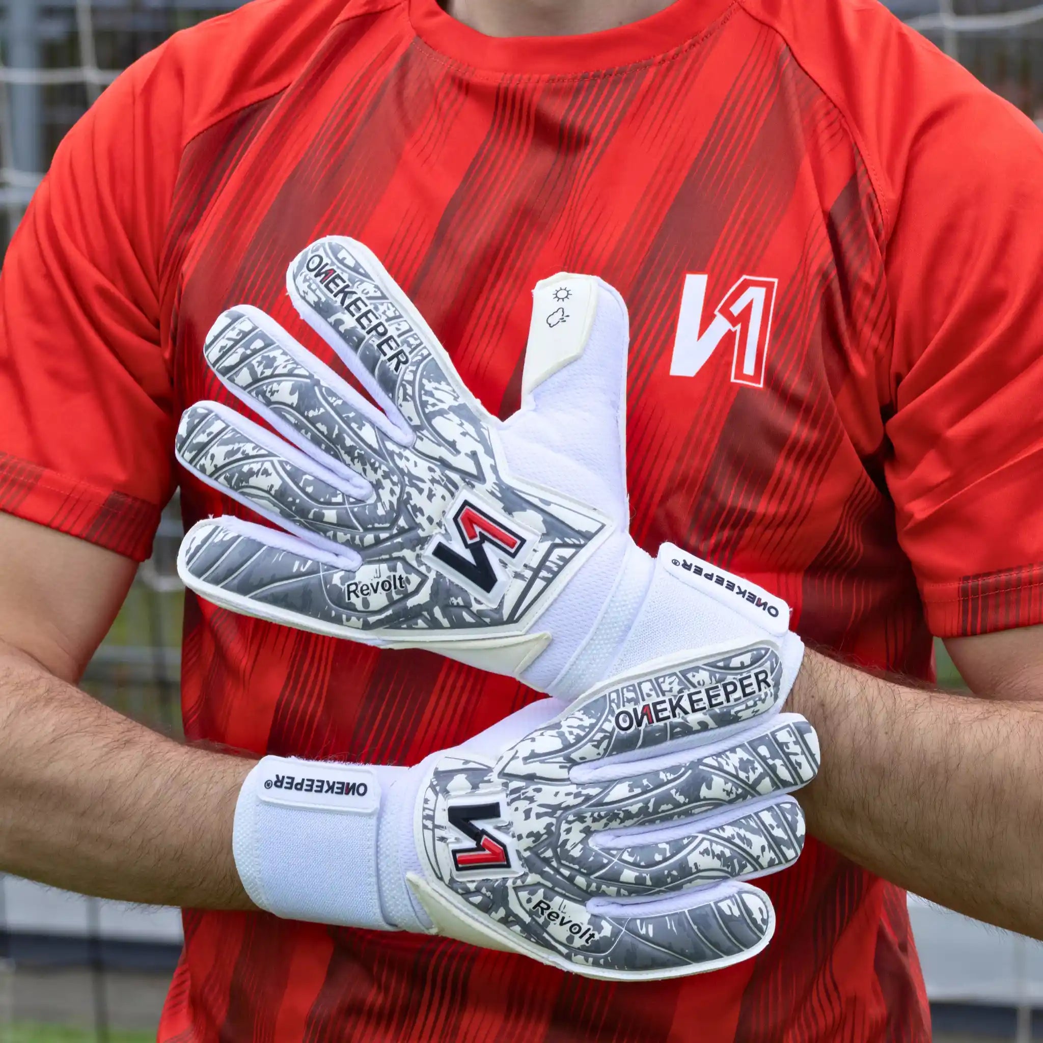 Person wearing red sports jersey and a onekeeper revolt white goalkeeper gloves with visible branding.