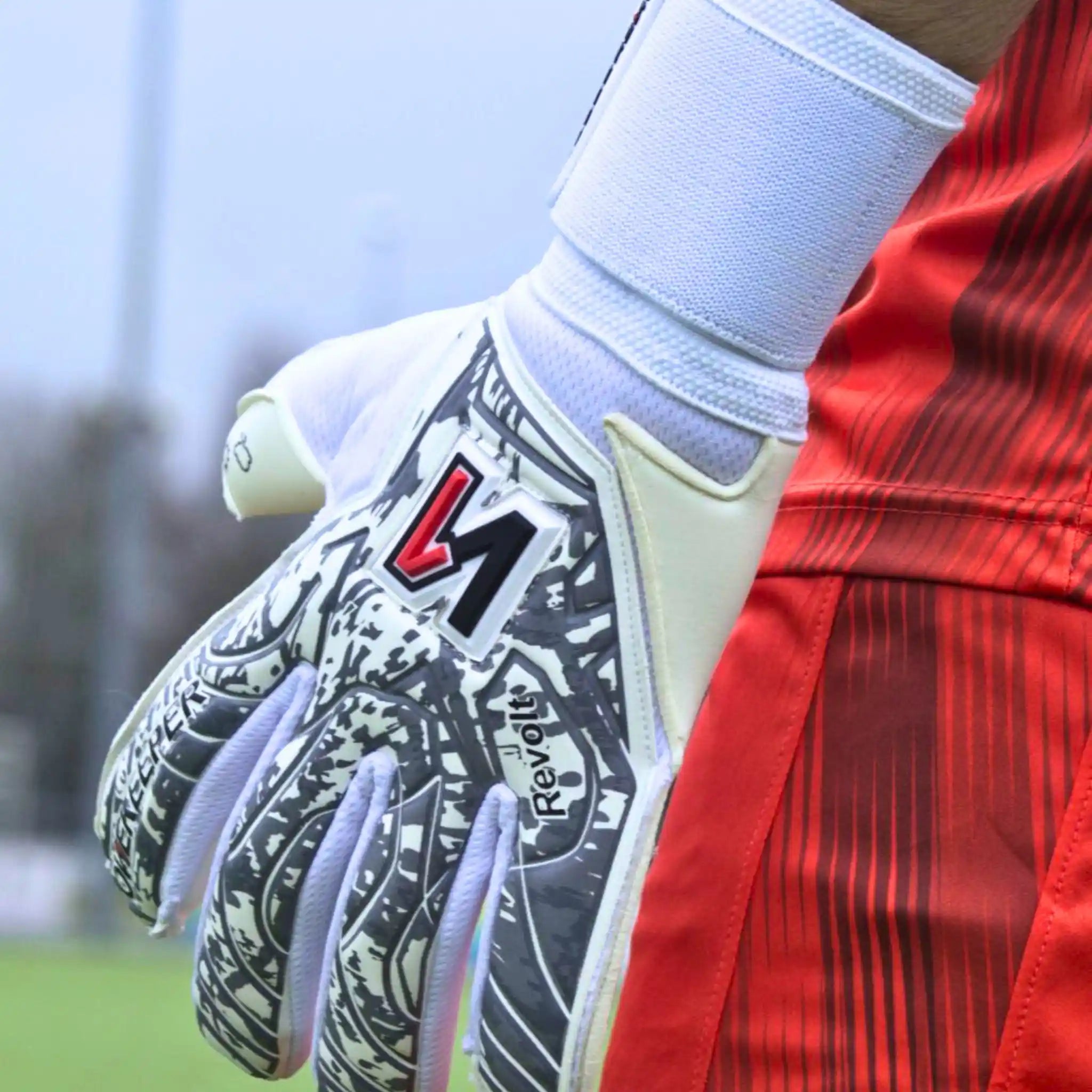 Close-up of a soccer onekeeper revolt white goalkeeper's glove with a brand logo, wearing a red jersey.