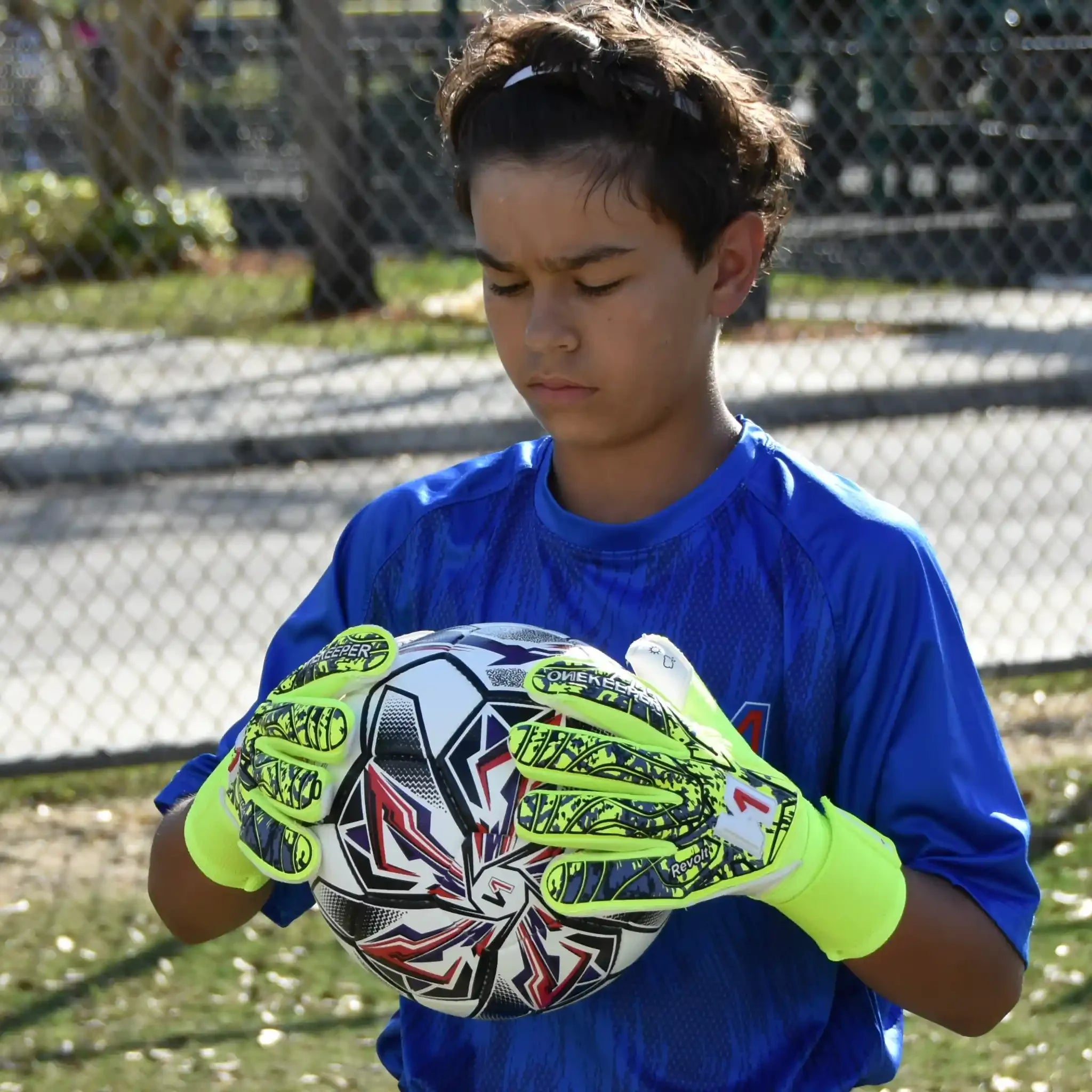 Child holding a soccer ball wearing a onekeeper revolt fluo yellow gloves on a grassy field