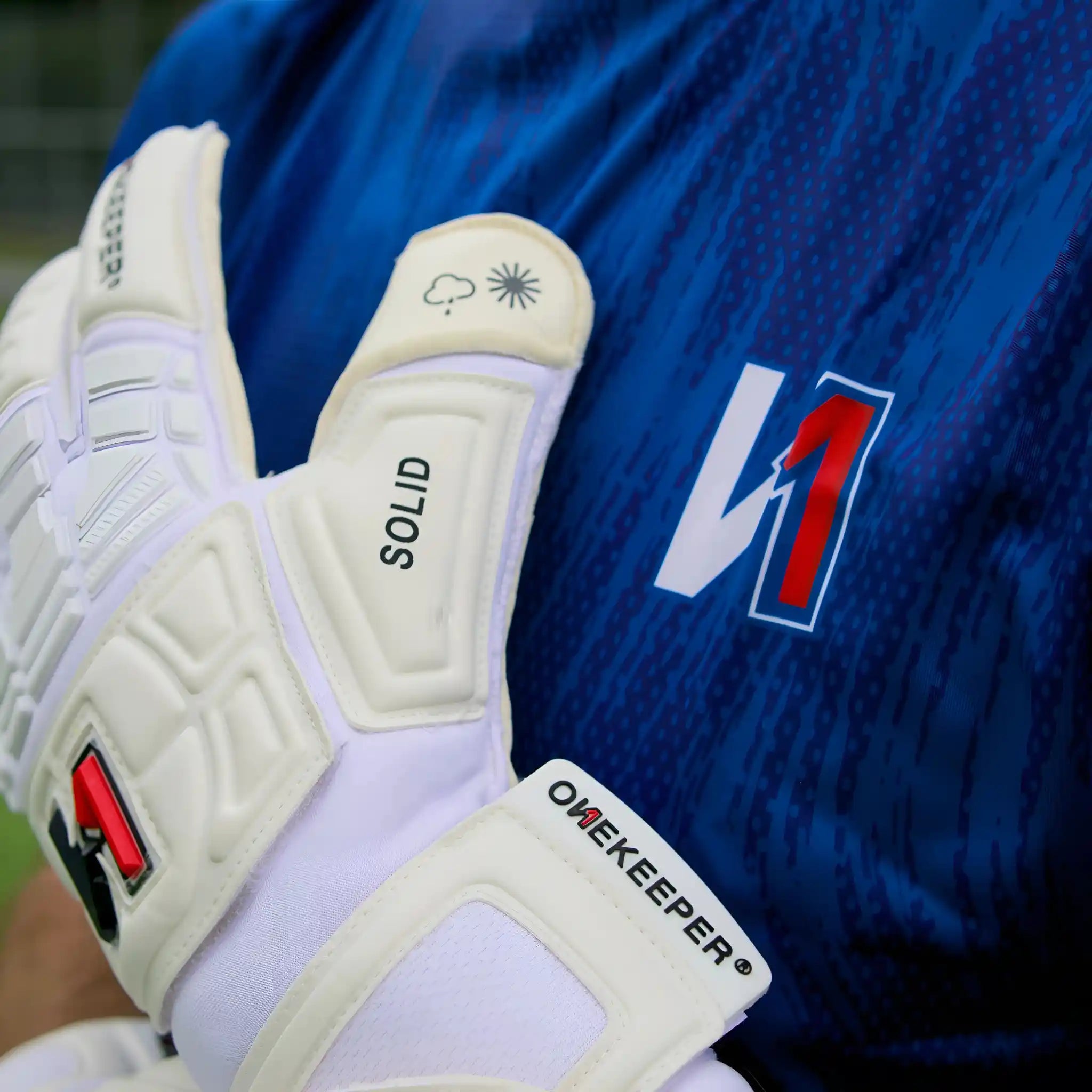 ONEKEEPER Solid White goalkeeper glove with 'ONEKEEPER' branding on a blue sports jersey background