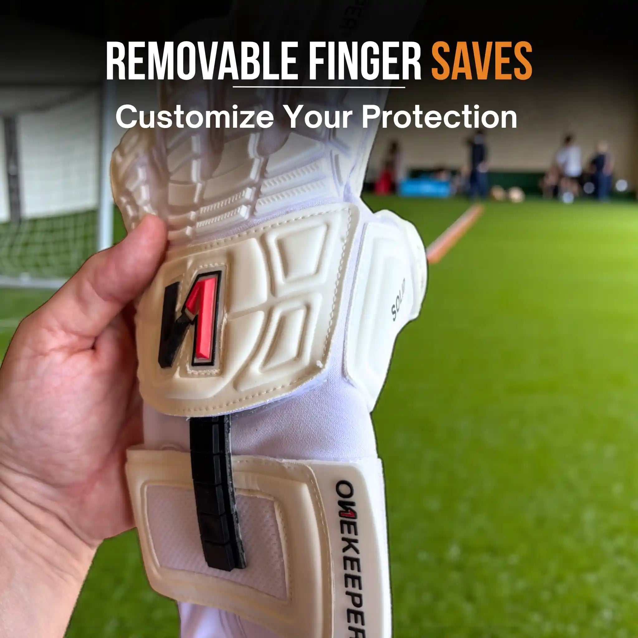 Hand holding a onekeeper solid white protective gear with 'ONEKEEPER' branding on a sports field background.