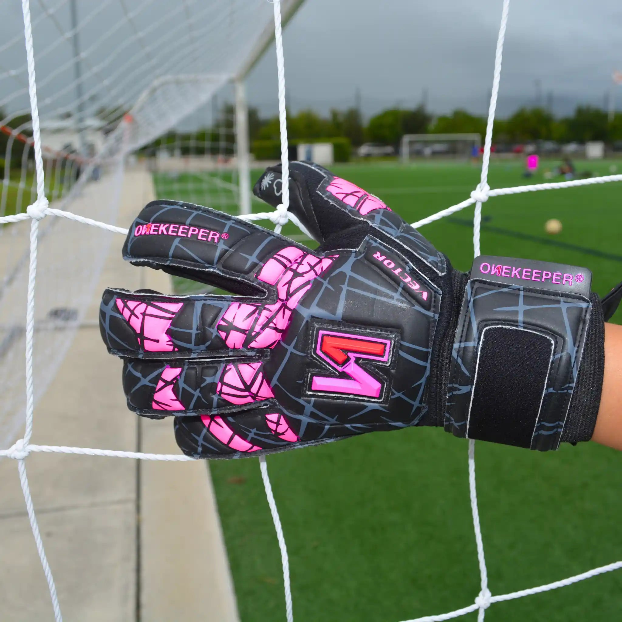 ONEKEEPER Vector EvolutionBlack and pink goalkeeper gloves with a brand logo on a soccer goal net background