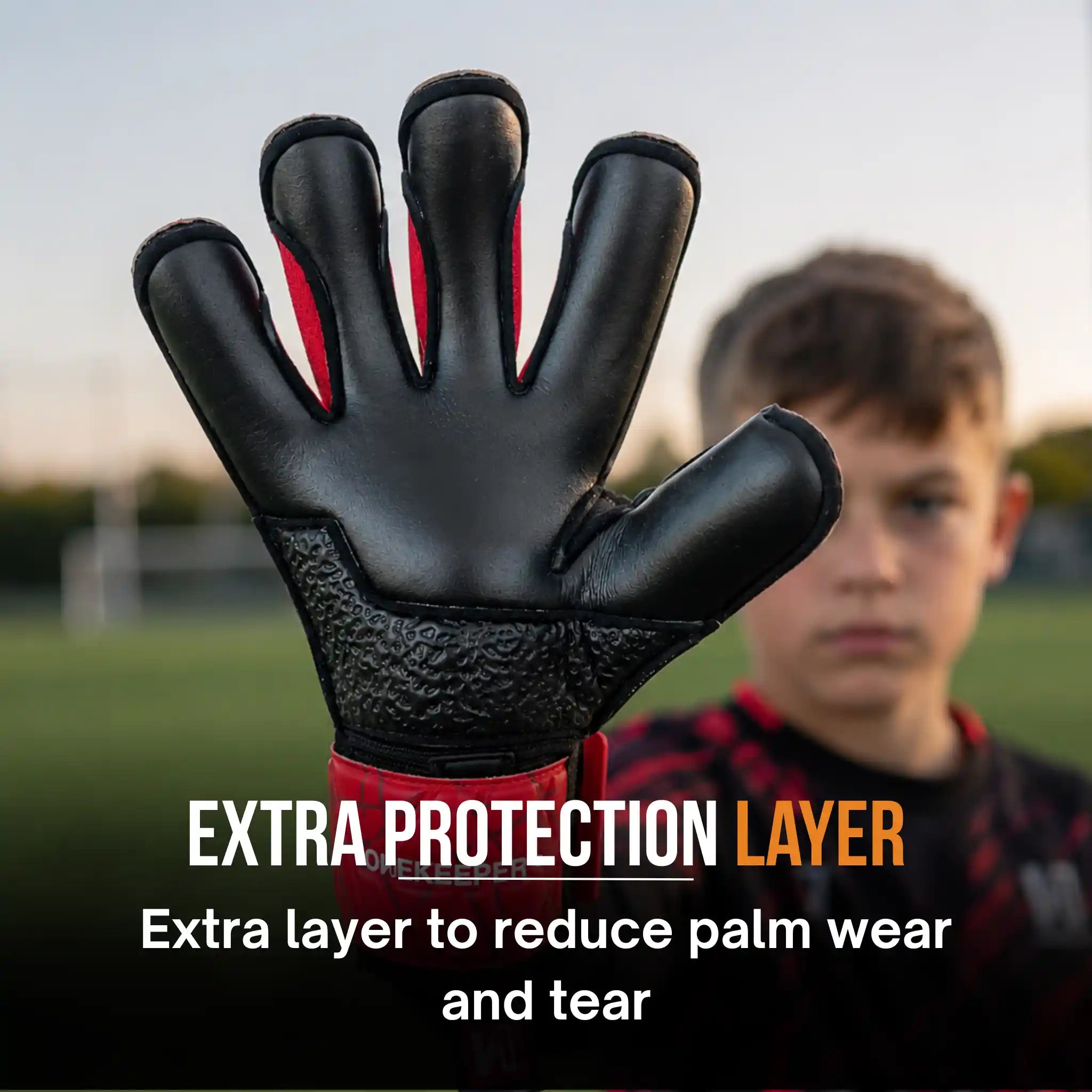 ONEKEEPER Vector Evolution Red and Black soccer glove with red accents on a blurred background of a child on a soccer field.