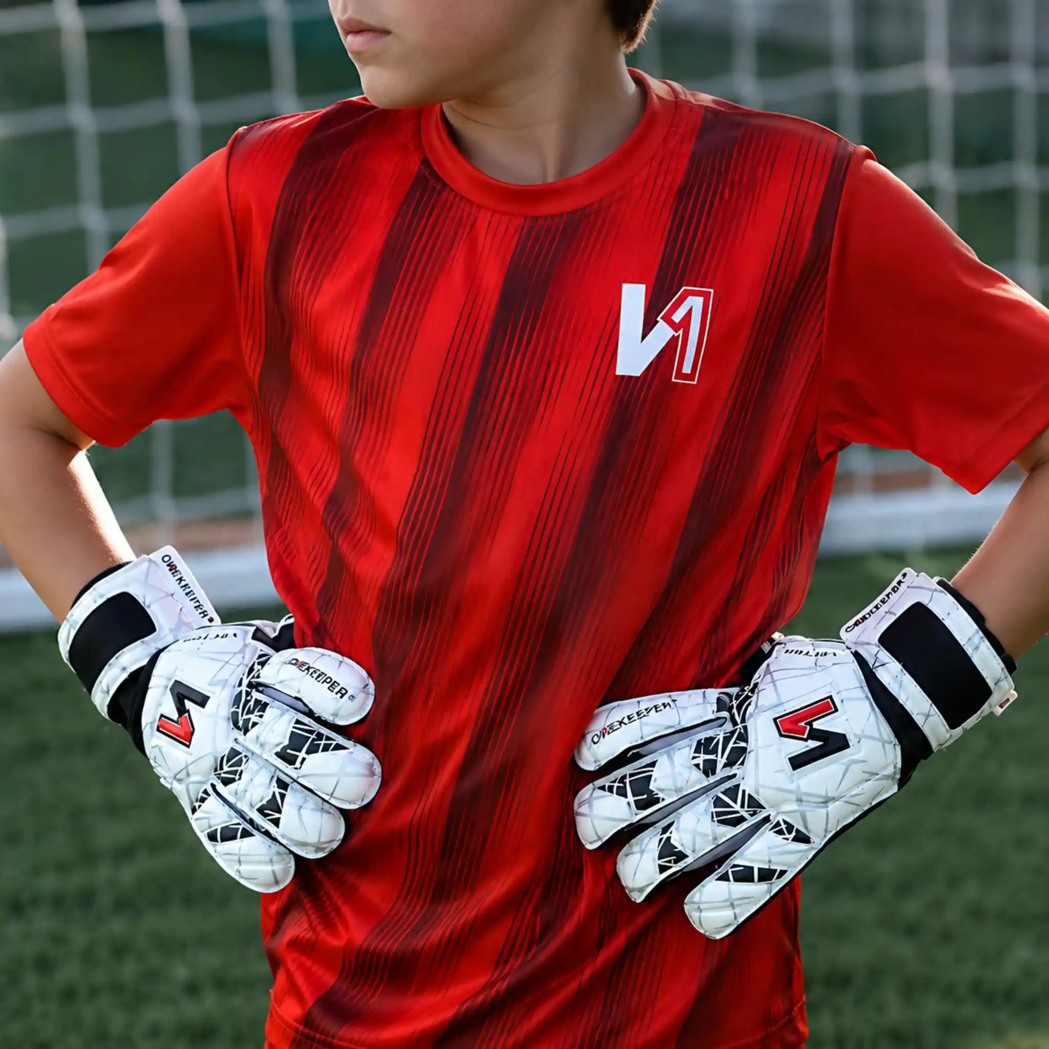 Child wearing a red sports jersey with a logo and a onekeeper vector evolution white and black gloves on a grassy field.