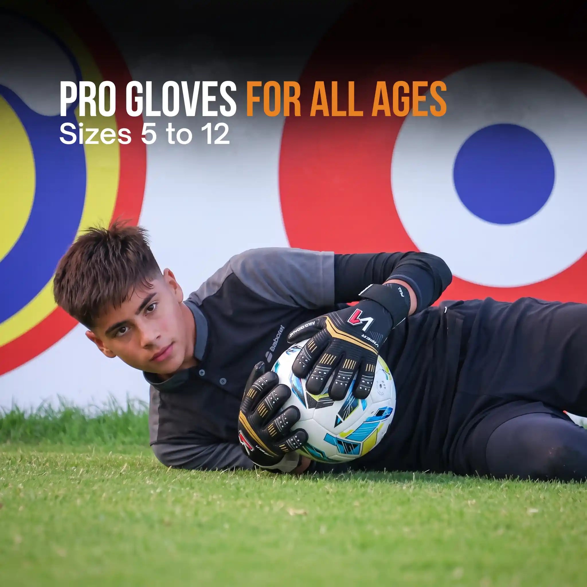 A young soccer goalkeeper lying on grass wearing a onekeeper viper black and gold black and gray training gloves and holding a soccer ball, with large text reading 'PRO GLOVES FOR ALL AGES' and 'Sizes 5 to 12' over a blurred target backdrop.