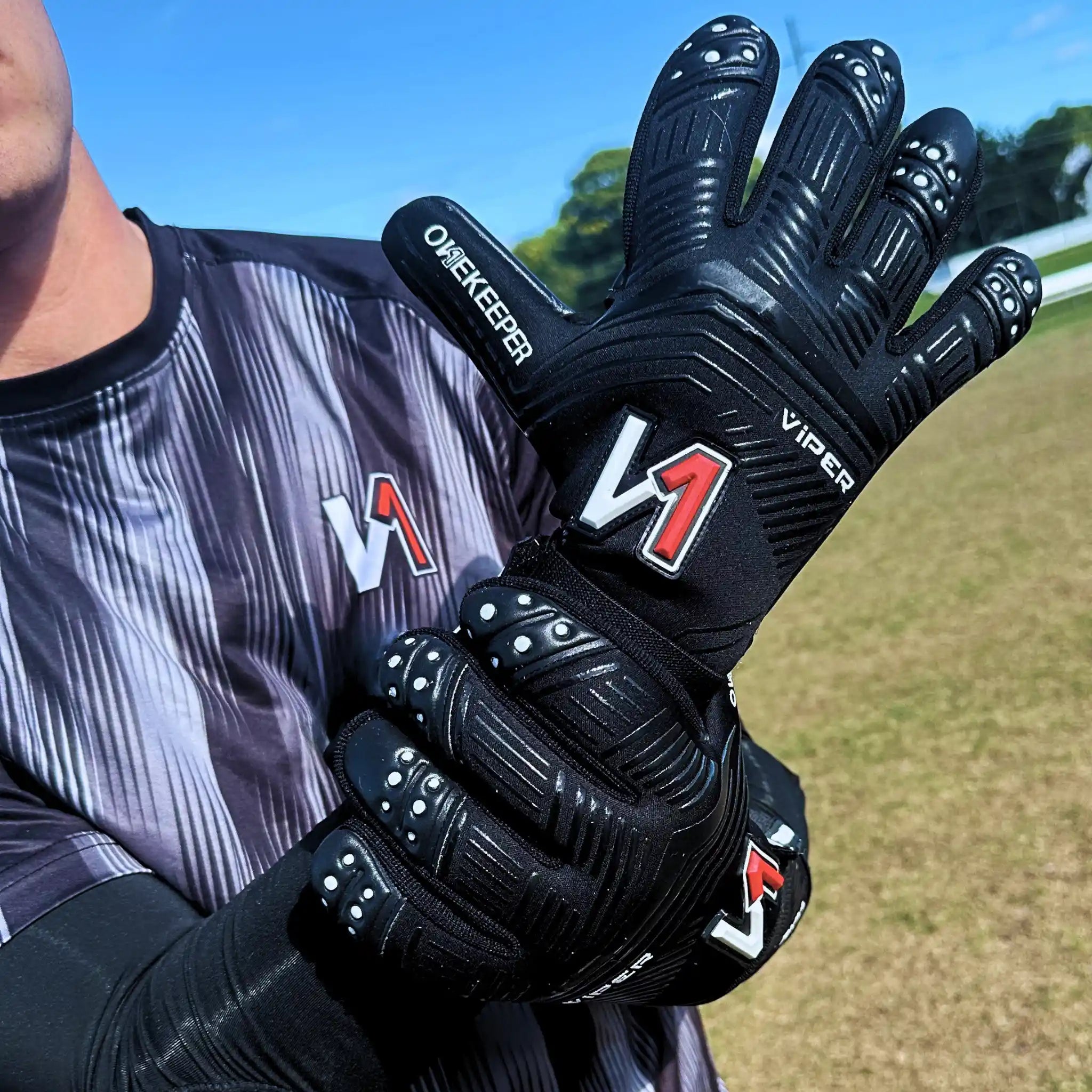 onekeeper viper Black goalkeeper gloves with Viper branding held by a person on a sports field.