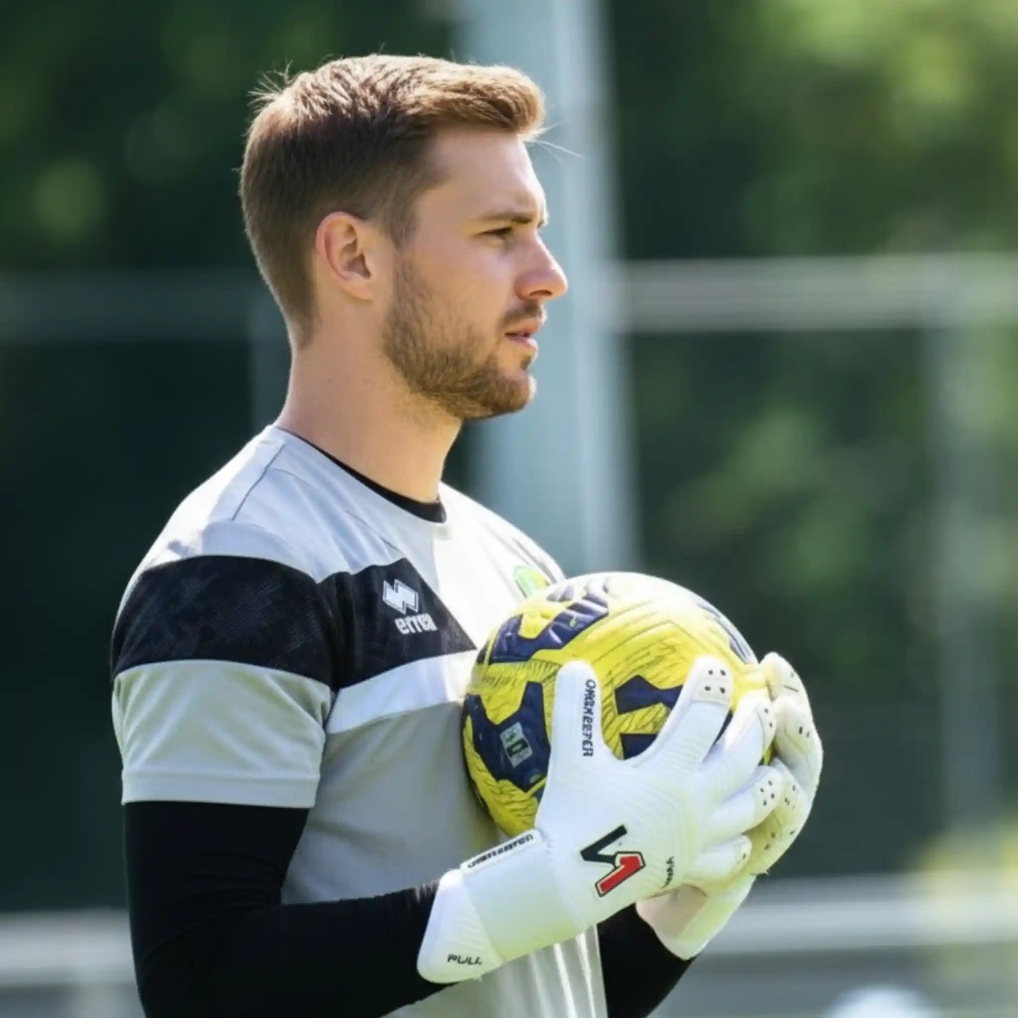 Man holding a soccer ball on a sports field with a onekeeper viper white gloves.