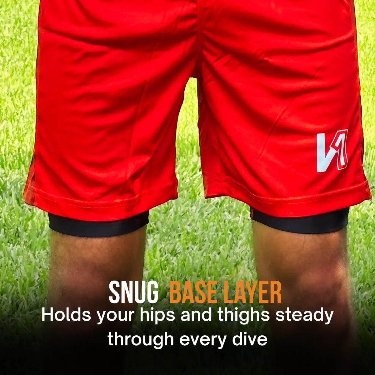 Close-up of a person wearing bright red athletic shorts over black onekeeper compression-style base layers, standing on grass with text overlay reading 'SNUG BASE LAYER' and 'Holds your hips and thighs steady through every dive'.